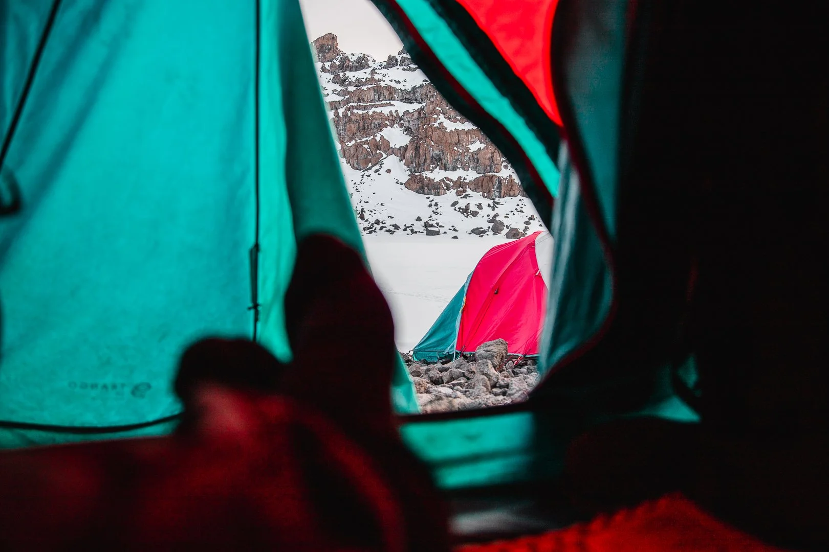 View from inside a tent looking out at snow-covered ground and distant mountains with rocky cliffs.