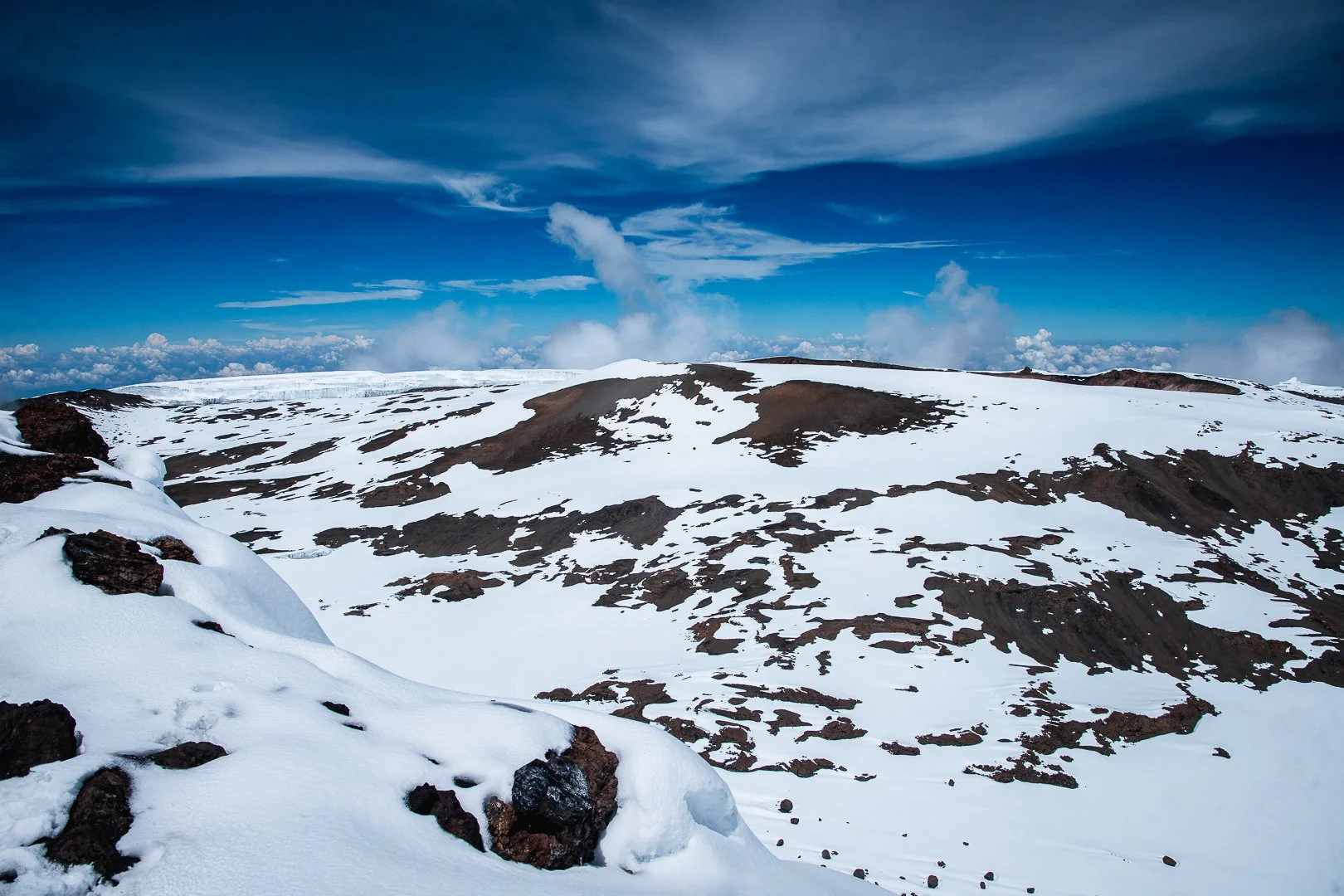Snow-covered mountain landscape under a partly cloudy blue sky with dark rocky patches.