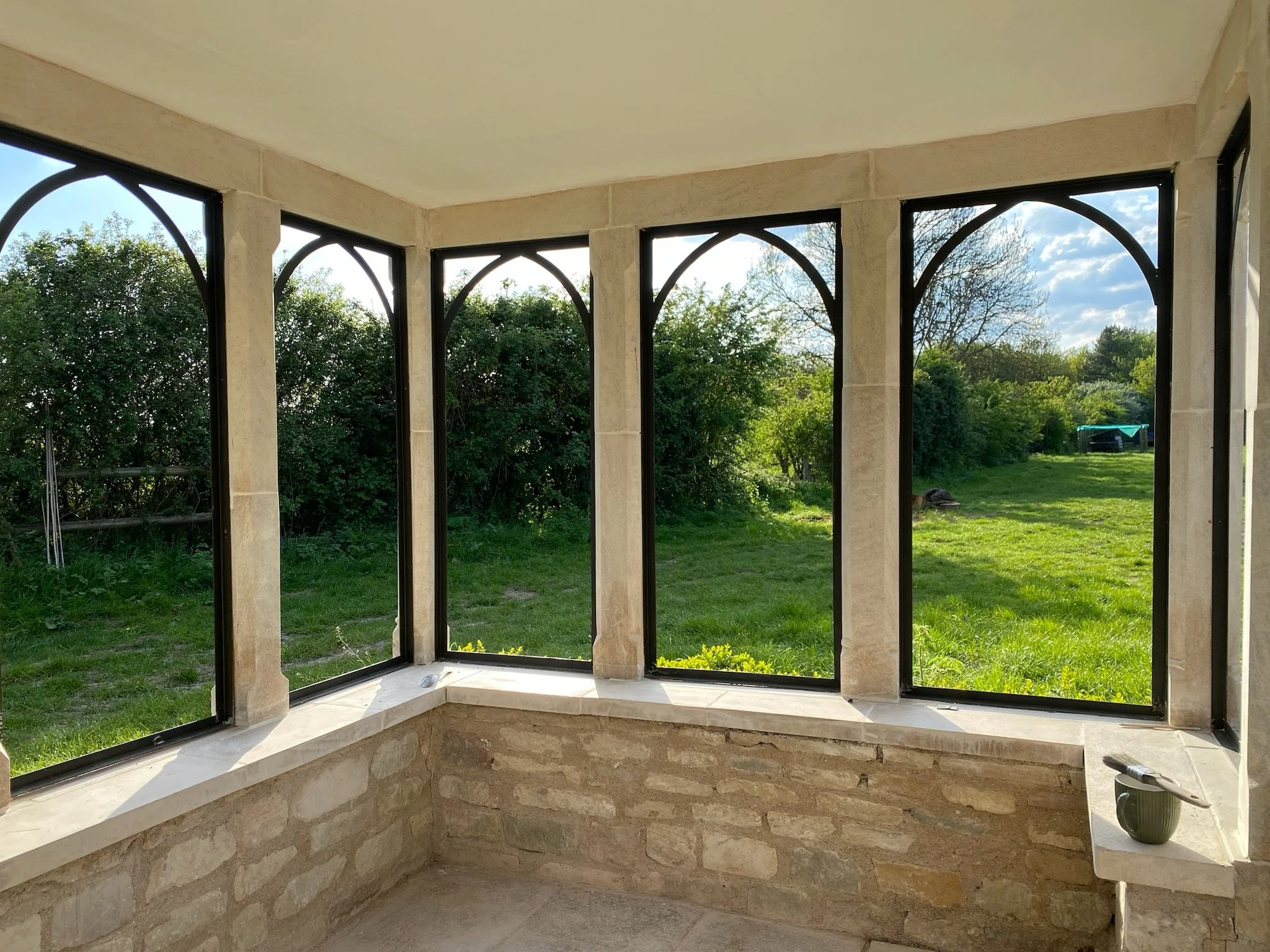 A view from inside a mullion house stone building looking out to the garden, the windows are black and medieval styled with arches