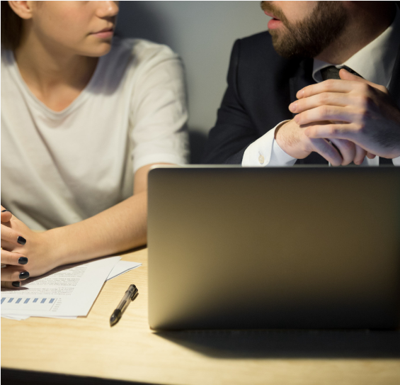 Two people having a serious discussion during a business meeting, with a laptop and documents on the table.