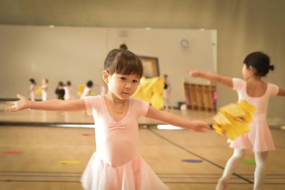Young girls in pink ballet dresses practicing with yellow pom-poms in a dance studio.