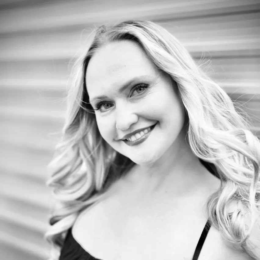 Black and white portrait of a smiling woman with long, wavy hair, against a background with horizontal lines.