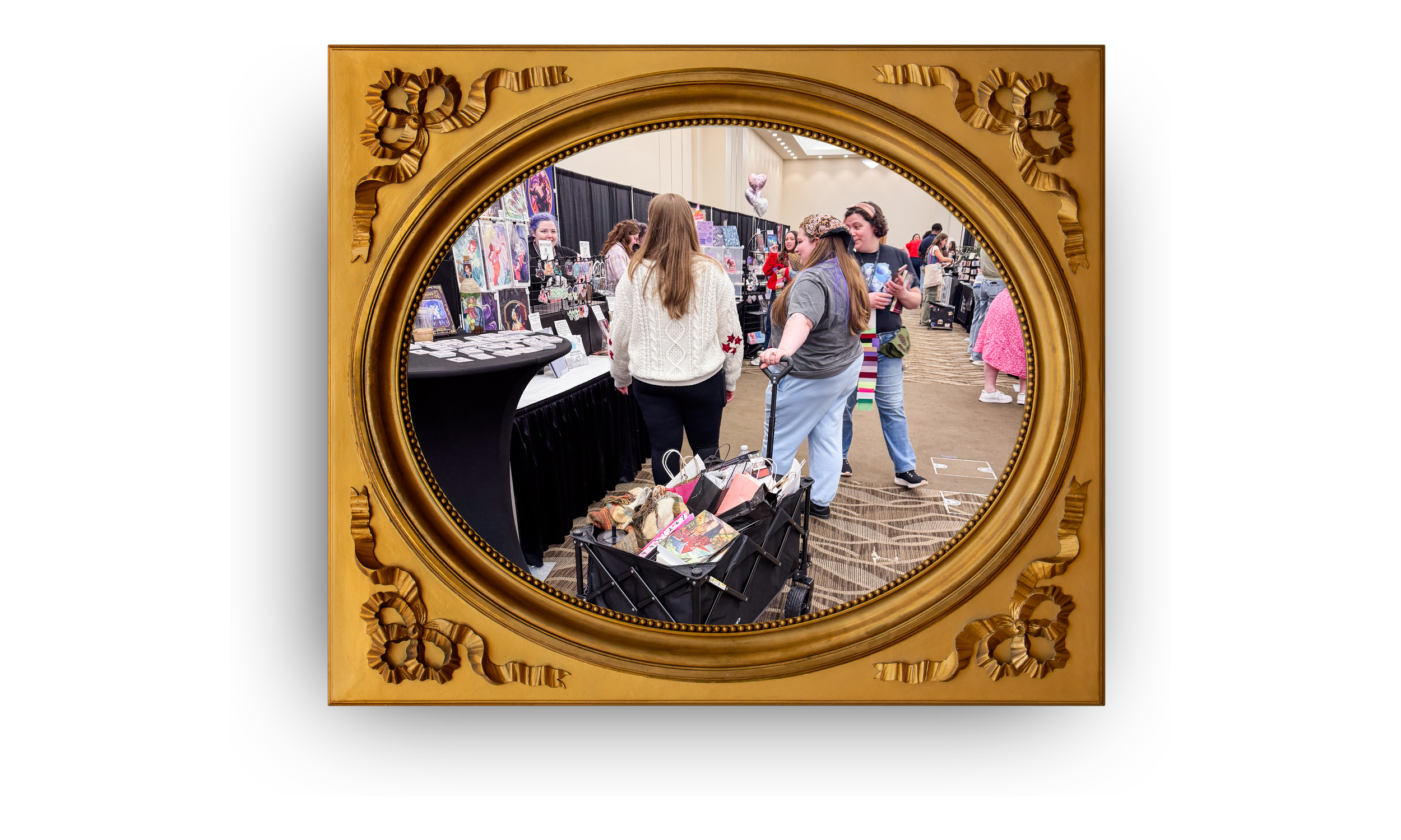 People at a vendor booth with artwork and accessories at an indoor event, seen through an ornate oval mirror.