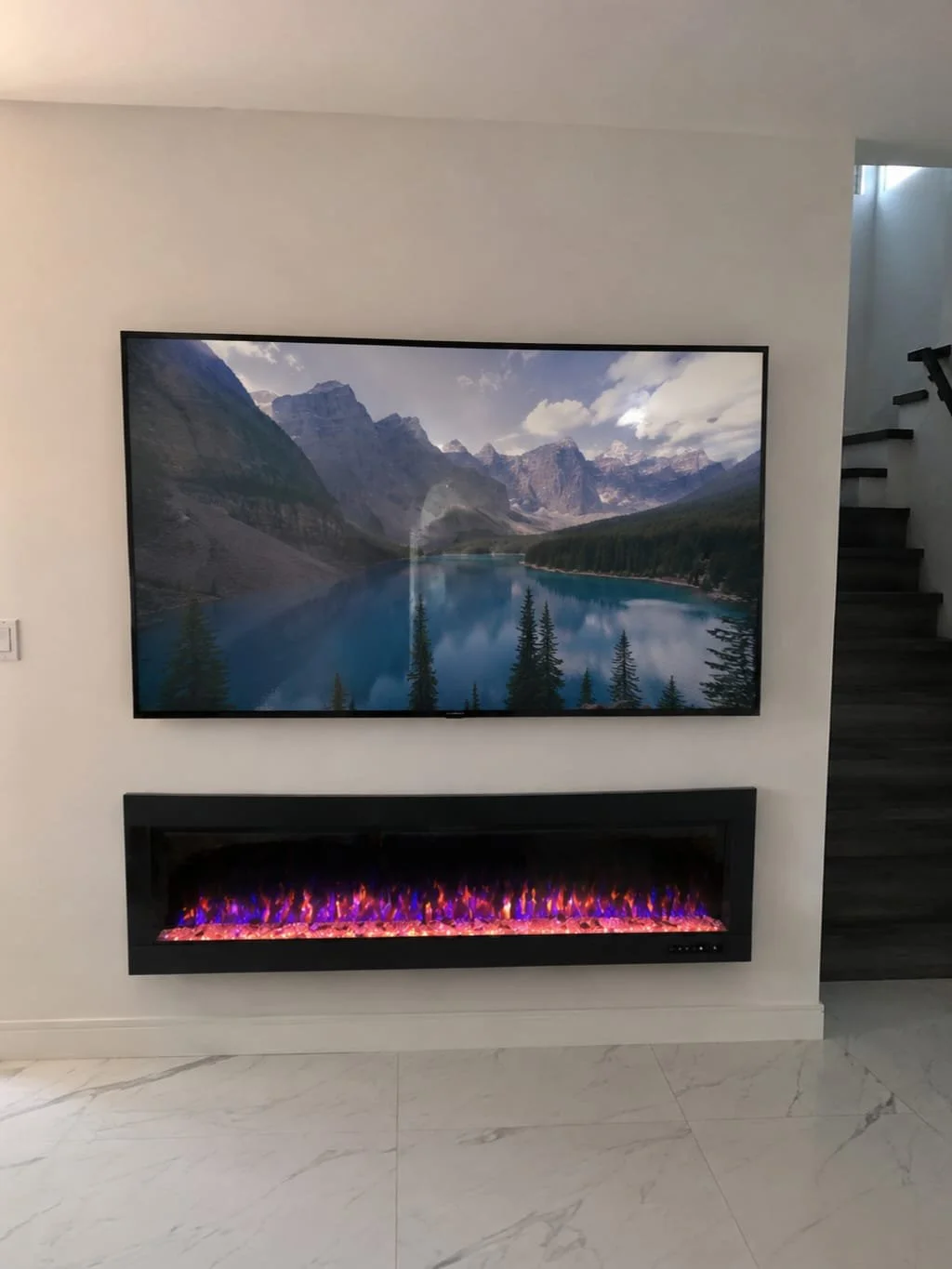 Écran affichant un paysage montagneux avec un lac et des arbres, placé au-dessus d une cheminée électrique en flammes.