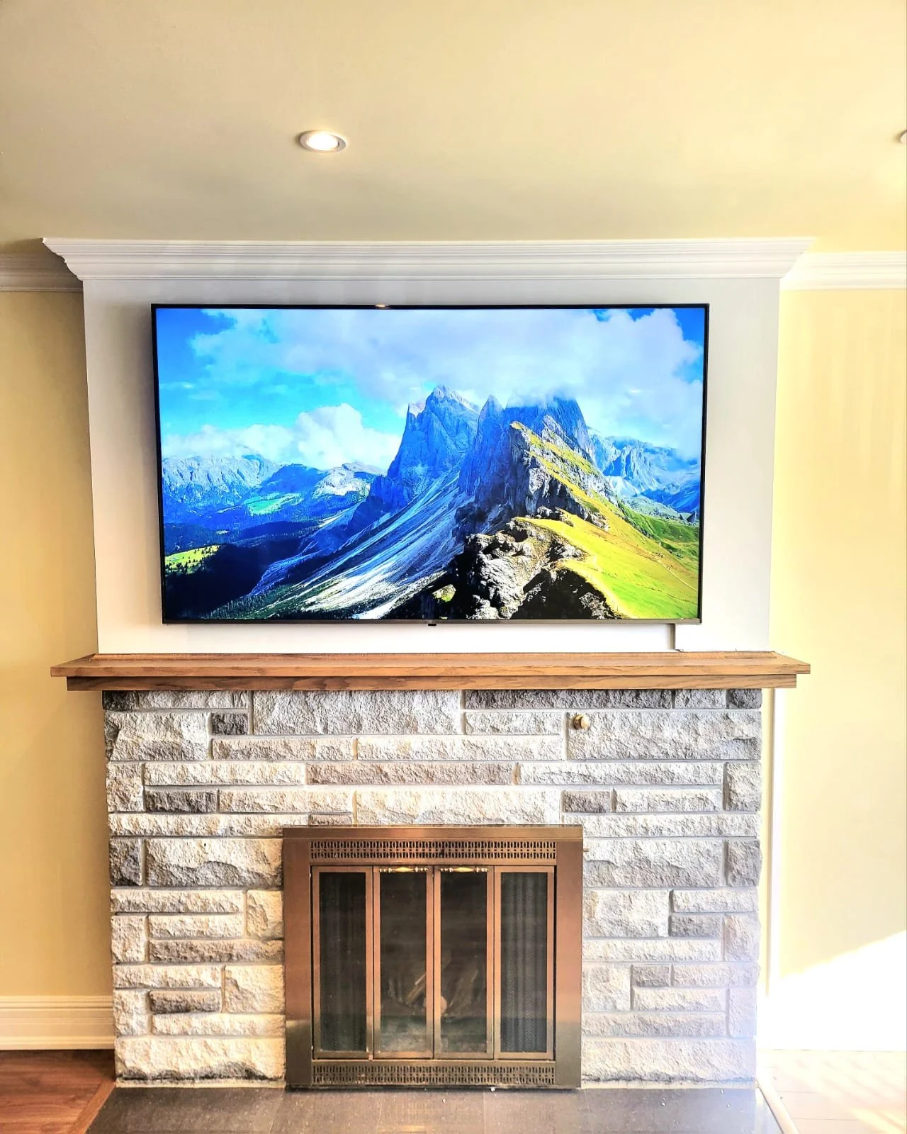Télévision affichant une montagne avec un ciel bleu, placée au-dessus d une cheminée en pierre avec un manteau en bois.