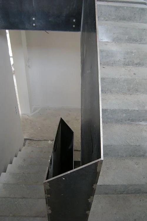 Innenaufnahme eines Treppenhauses mit schwarzen Metallgeländern und grauen Steinstufen.