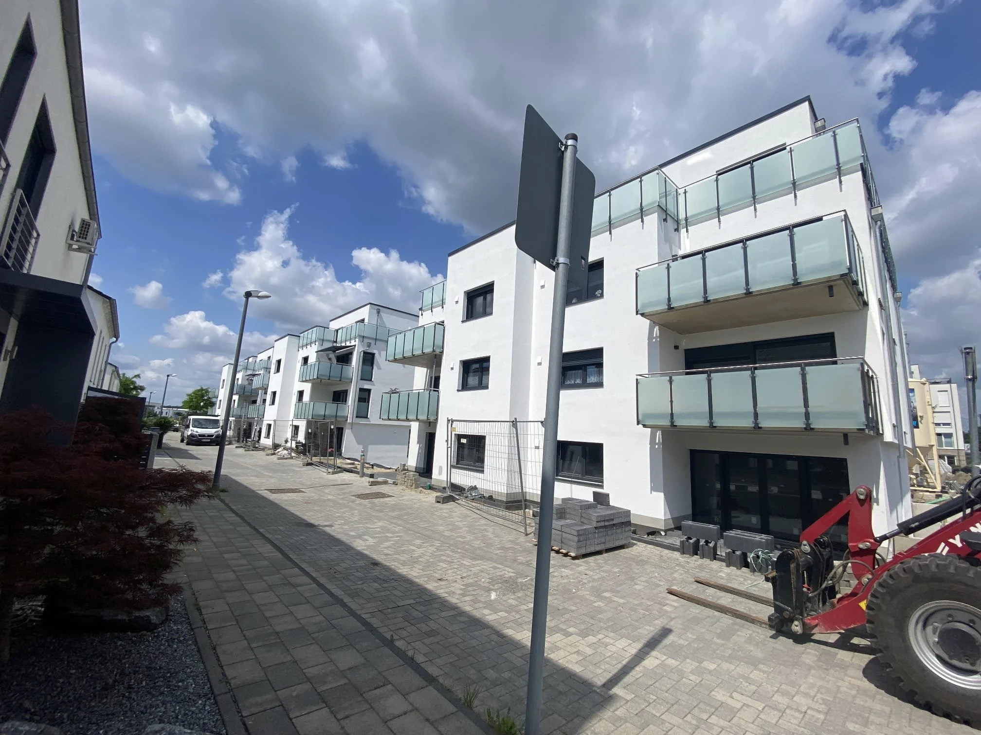 Ein moderner weiße Mehrfamilienhaus mit Balkonen und einer Baustelle im Vordergrund, auf der noch Arbeiten erfolgen, und der Himmel ist teils bewölkt.