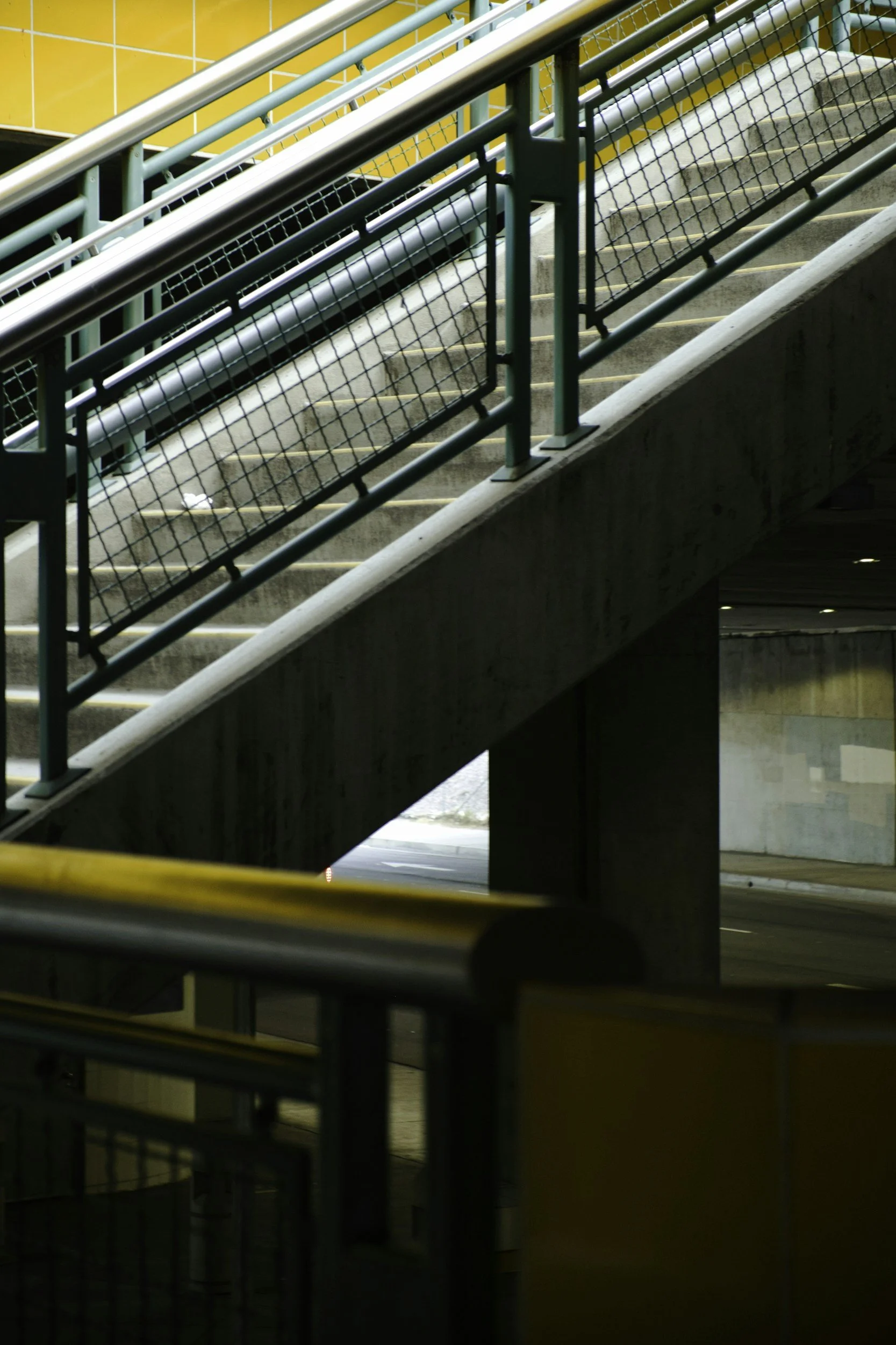 Blick auf eine Treppe mit Handläufen und Schutzgittern in einem Untergeschoss oder Tunnel.