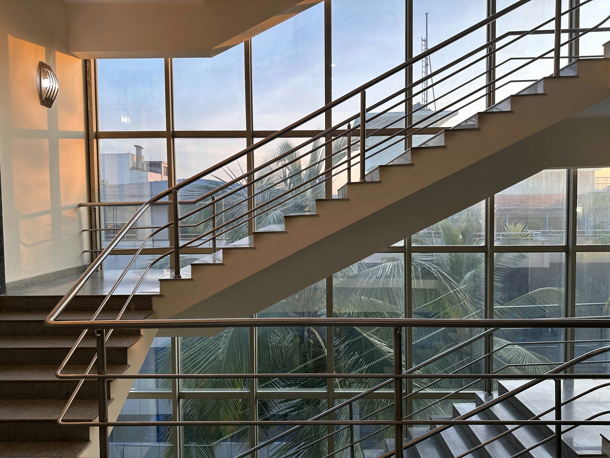 Innenansicht eines modernen Gebäudes mit einer Treppe, großen Glasfenstern und Blick nach draußen auf das Stadtbild und einen Himmel.