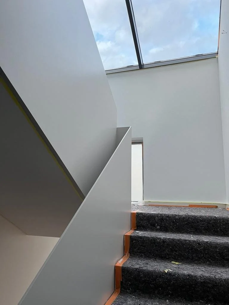 Innenaufnahme mit Treppenhaus, dunkle Teppichstufen, weiße Wände, Oberlichter im Dach.