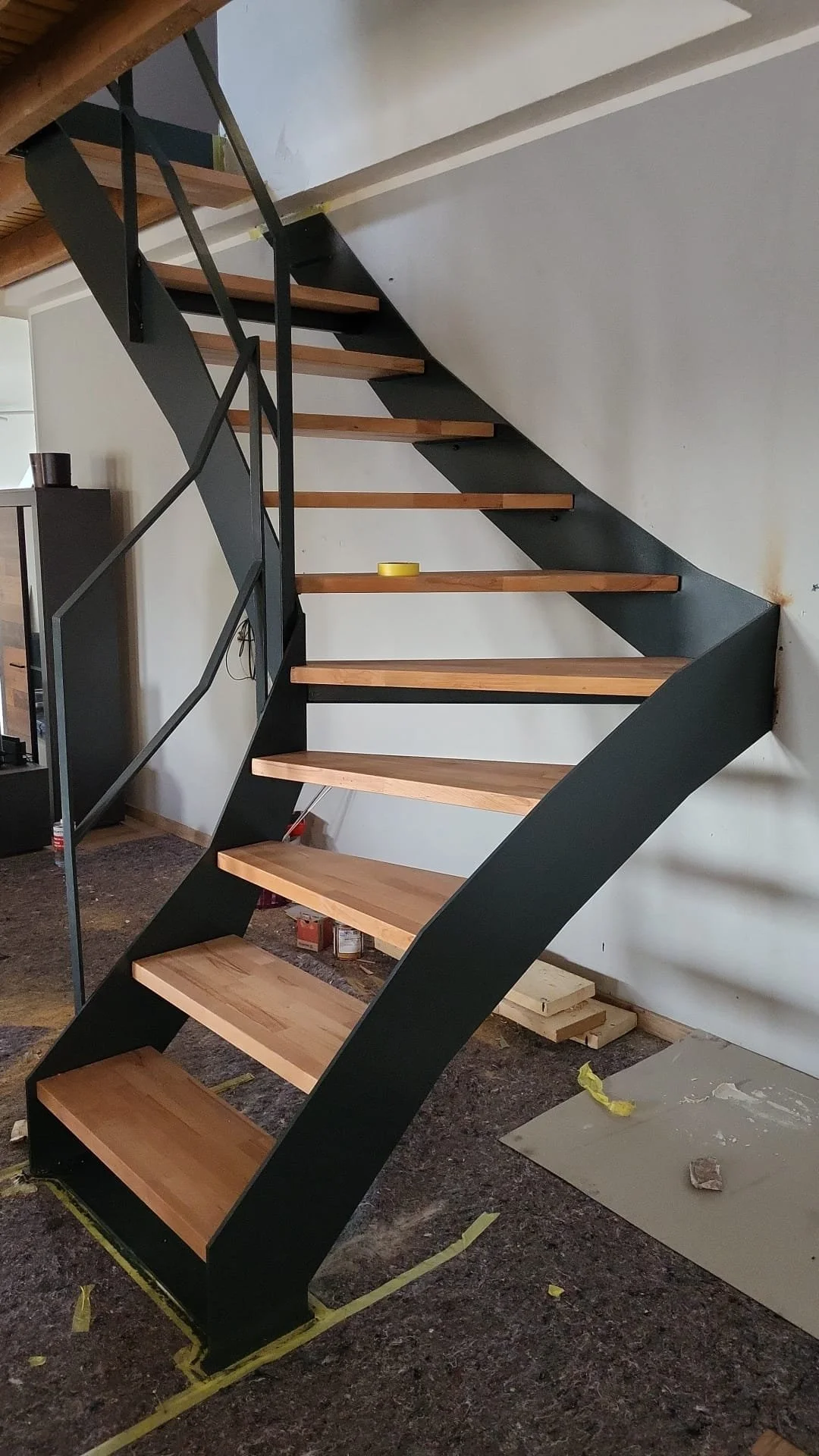 Ein moderner, offener Holz- und Metalltreppenaufgang in einem Wohnraum, noch im Bau.