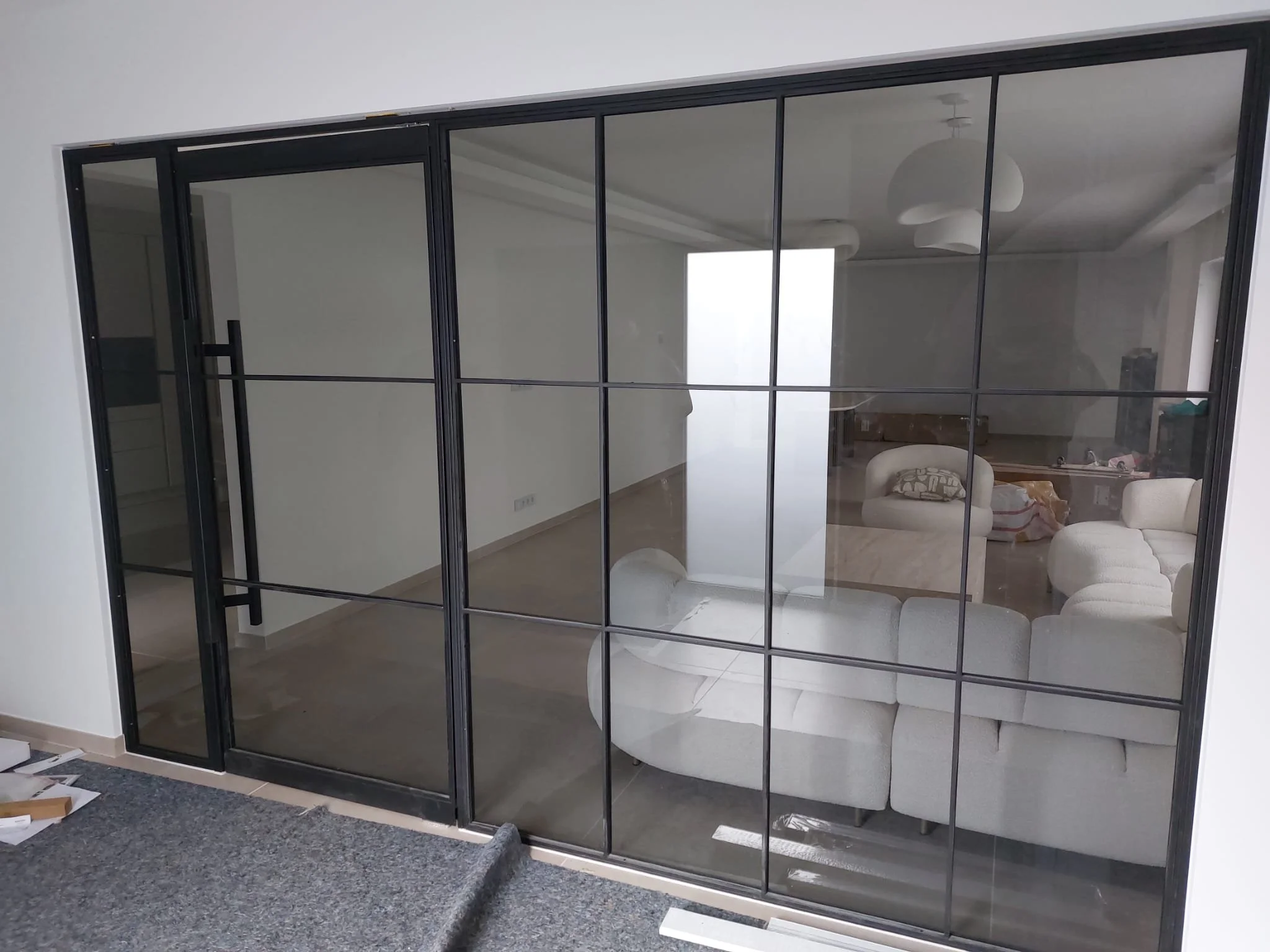Große schwarze Glastür im Innenraum,blick in ein Wohnzimmer mit weißen Sofa und Sofastuhl, innenarchitektur mit moderner Beleuchtung und weißen Wänden
