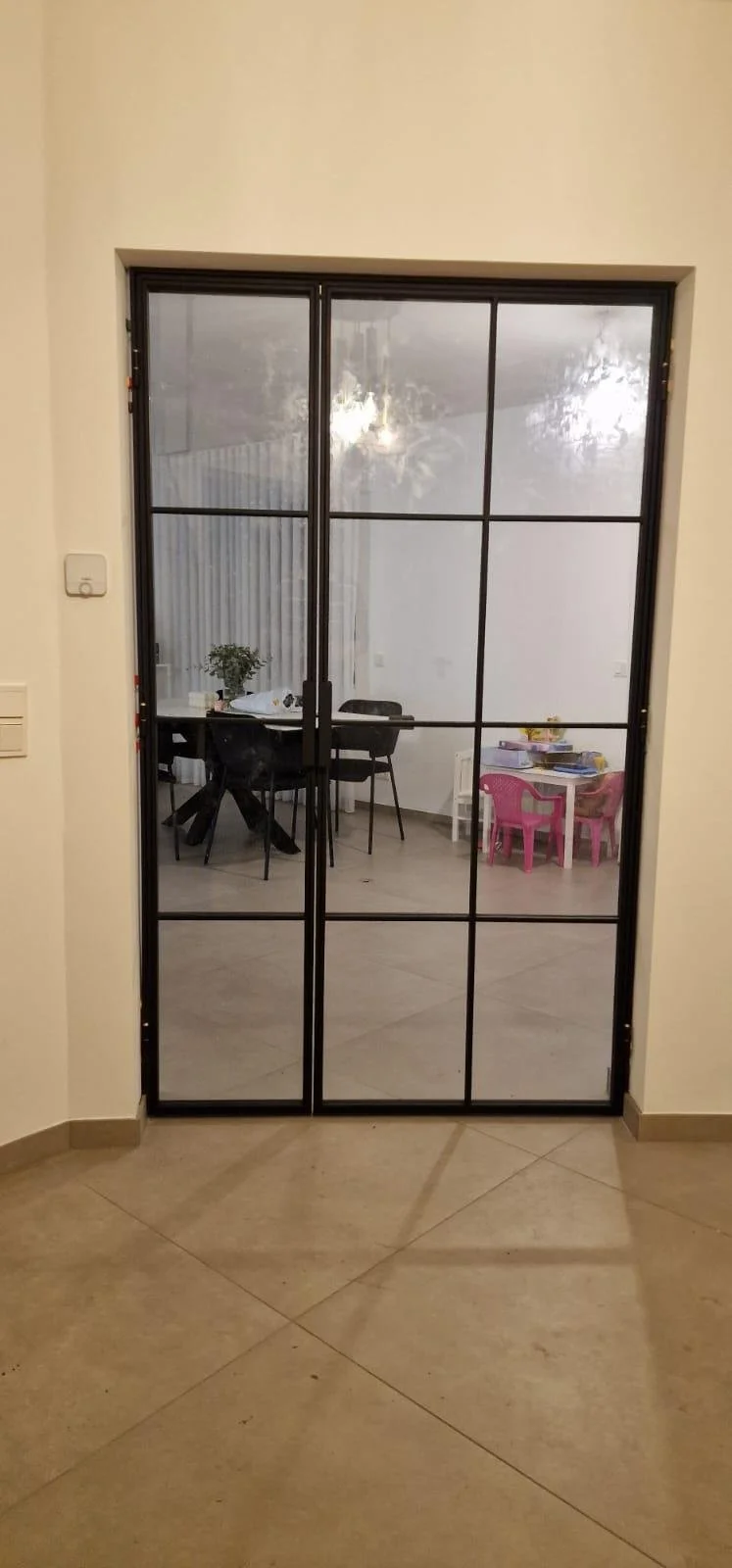Blick durch eine Glastür auf einen Essbereich mit einem Tisch, Stühlen und einer kleinen Kindertischgruppe in einem modernen Innenraum.