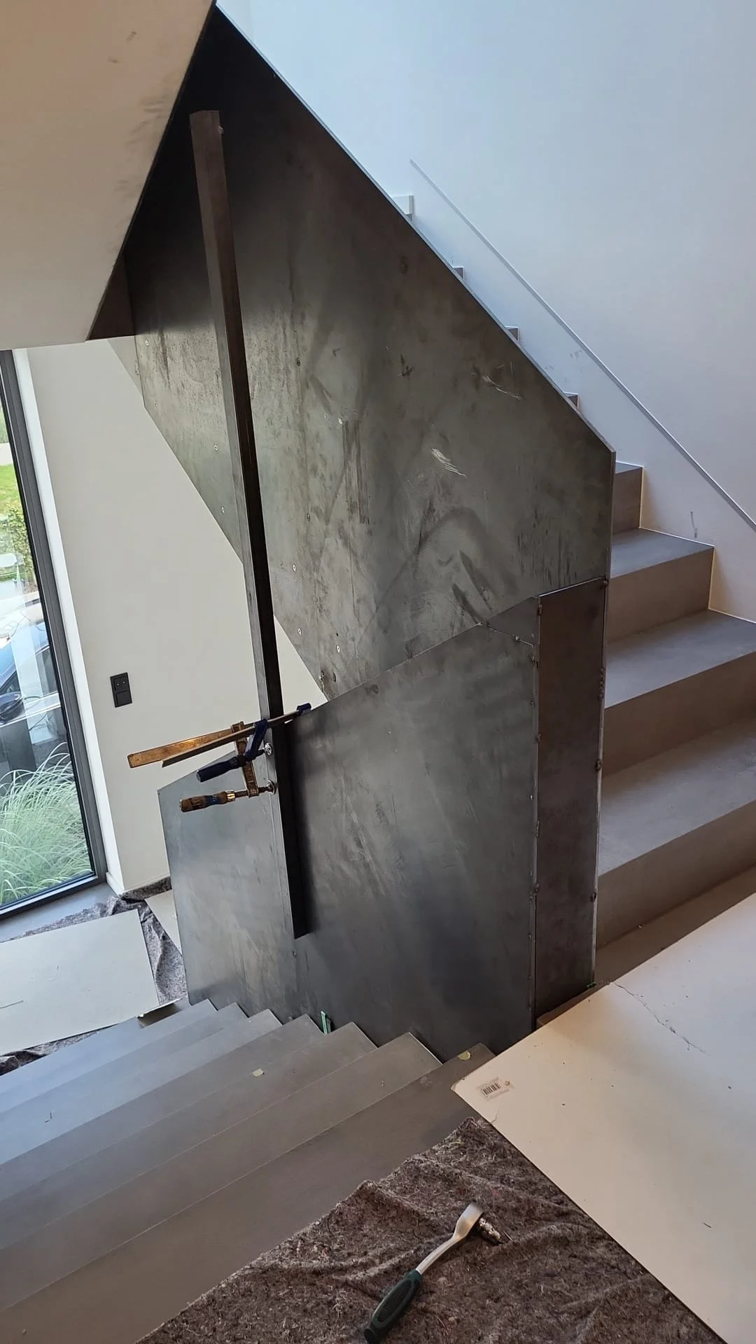 Der Verlauf einer Treppe mit einem neu installierten, metallischen Trennwand oder Schutzwand, die an der Seite der Treppe montiert wird. Es sind Werkzeuge, wie eine Klemme, sichtbar.