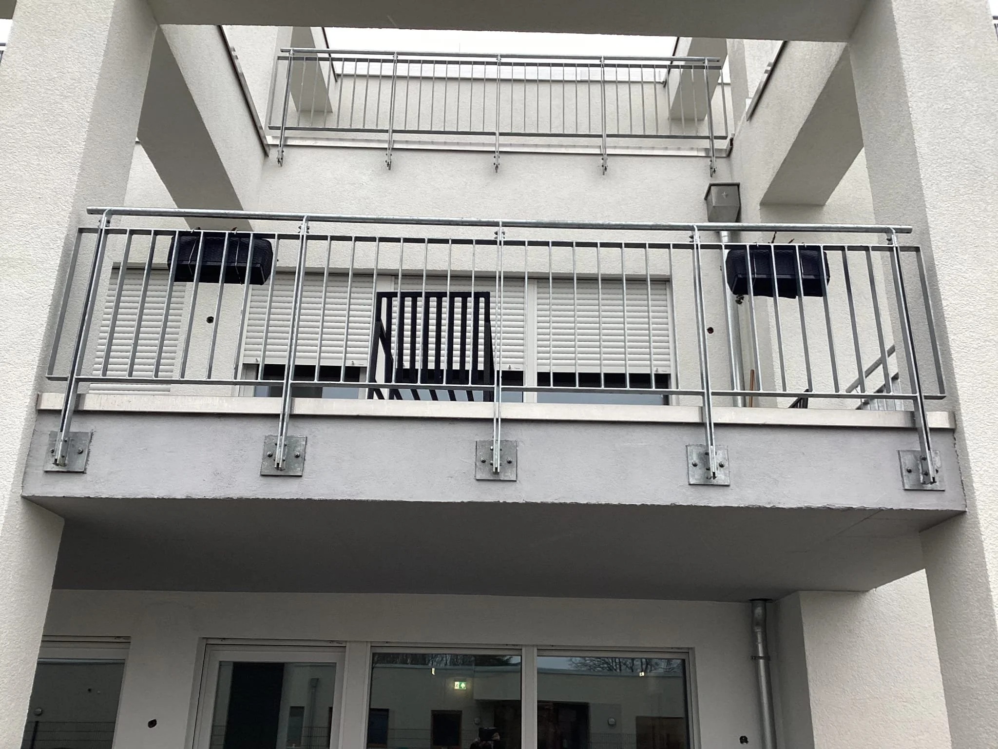 Mehrstöckige weiße Gebäude mit Balkon und Metallgeländer, Außenansicht.