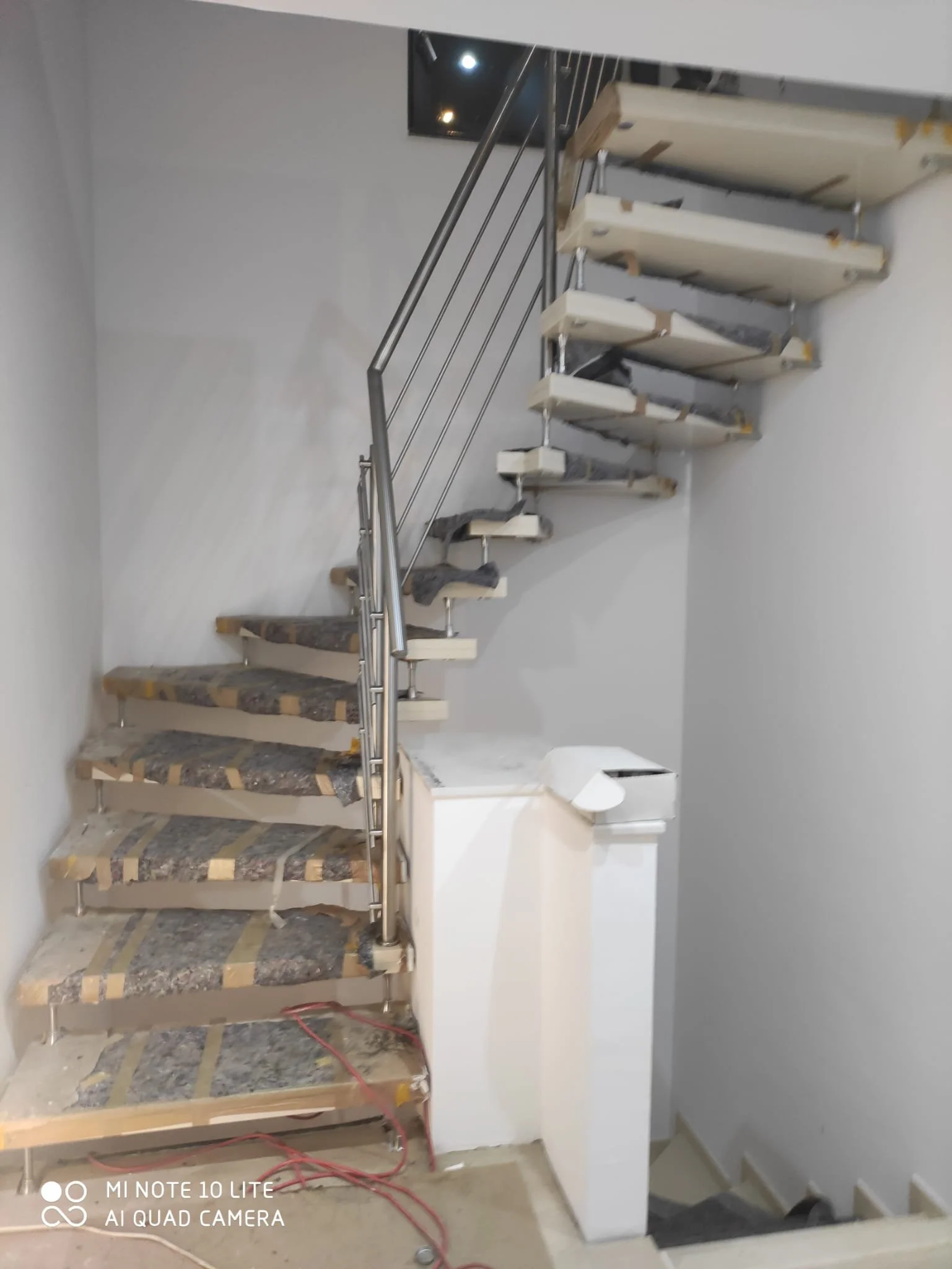 Innenansicht eines Hauses im Bau, gerade im Aufbaustadium mit einer Treppe, die noch nicht fertiggestellt ist, und einer weißen Zwischenwand. Die Treppe hat noch Schutzfolien auf den Stufen.