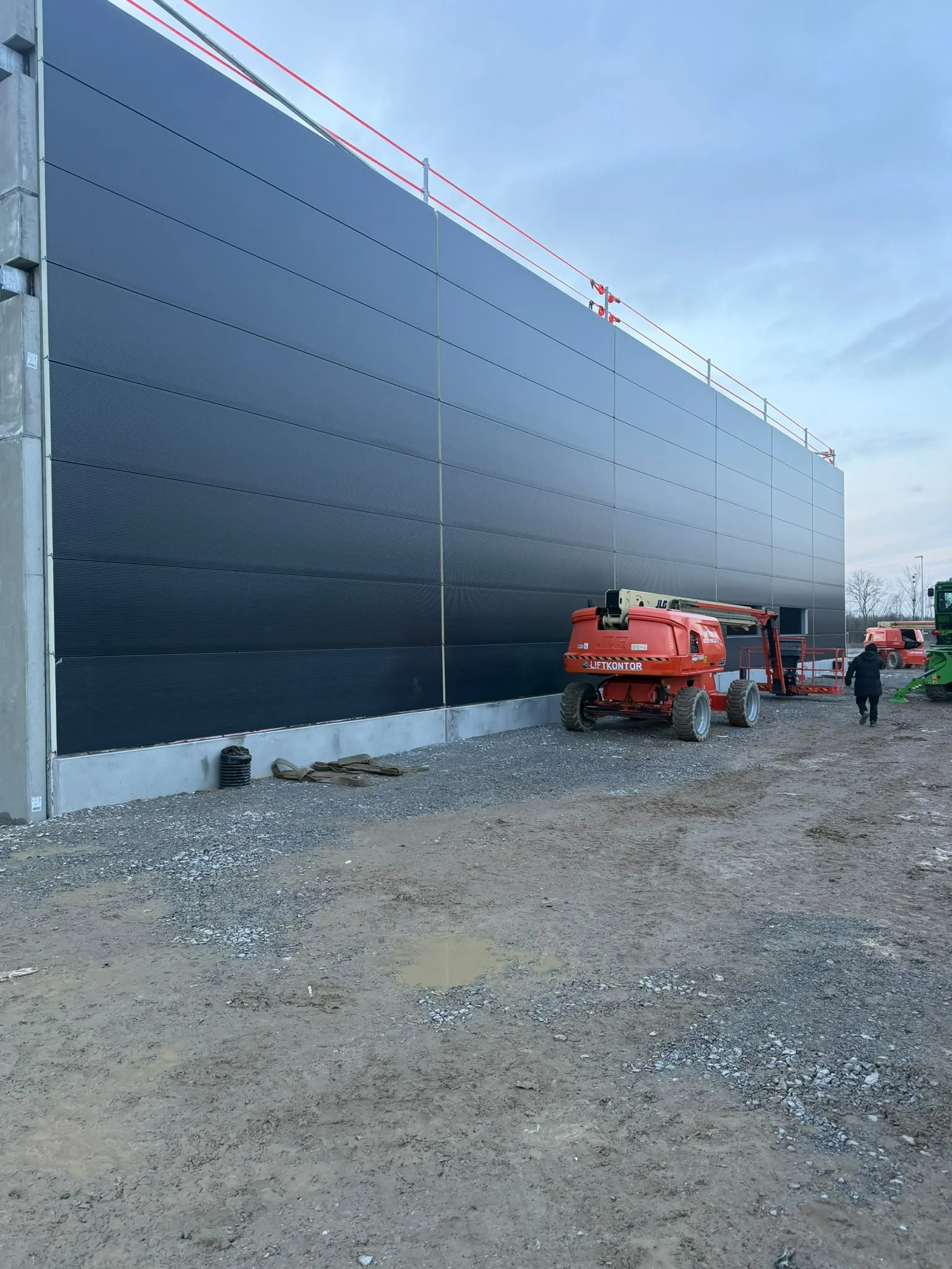 Baustelle mit einem roten Kran und einer Person, die sich auf einem unbefestigten Erdgelände befindet.