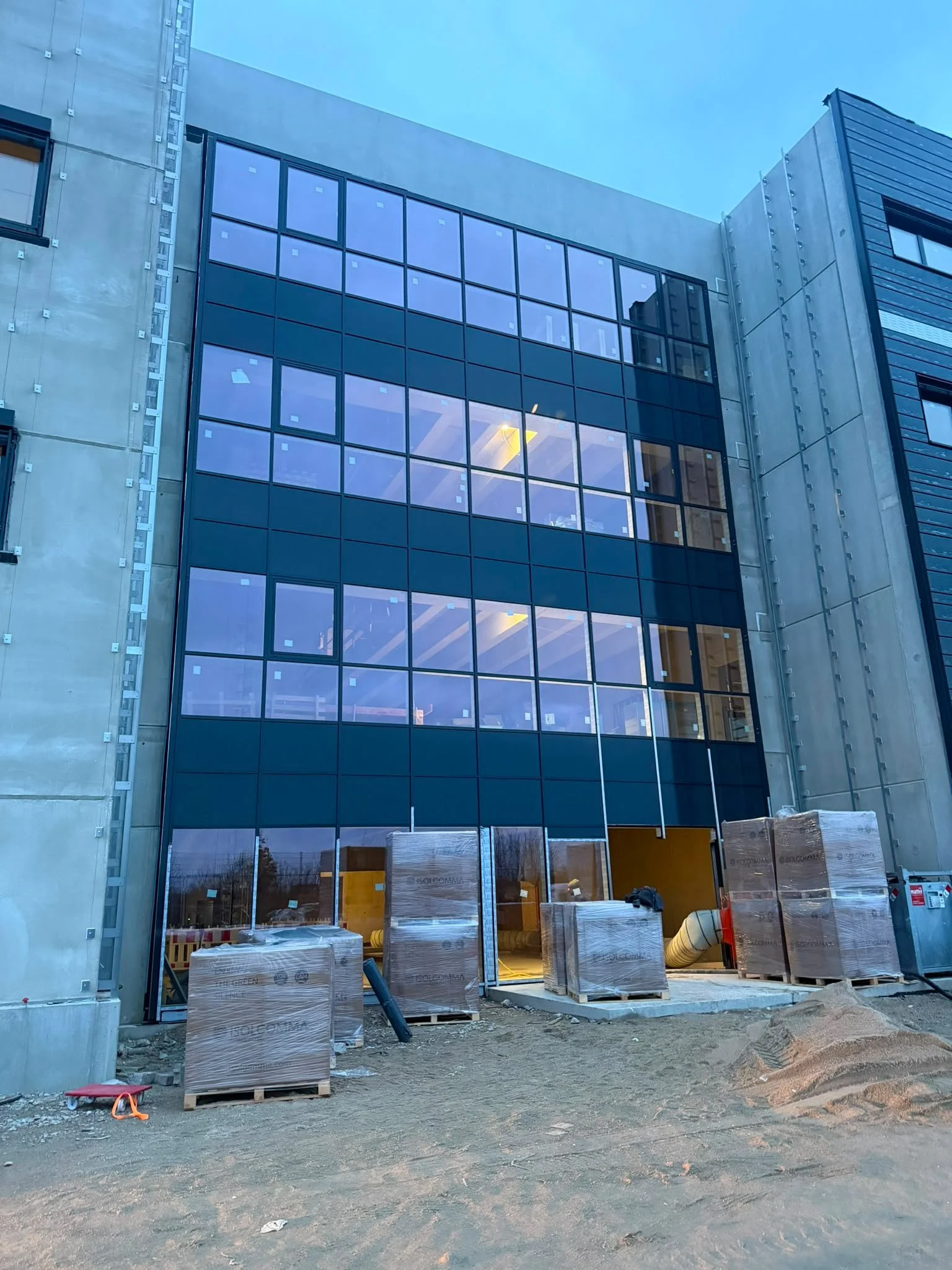 Baustelle eines modernen Gebäudes mit großer Fensterfront, Baumaterialien und Geräte auf dem unfertigen Boden
