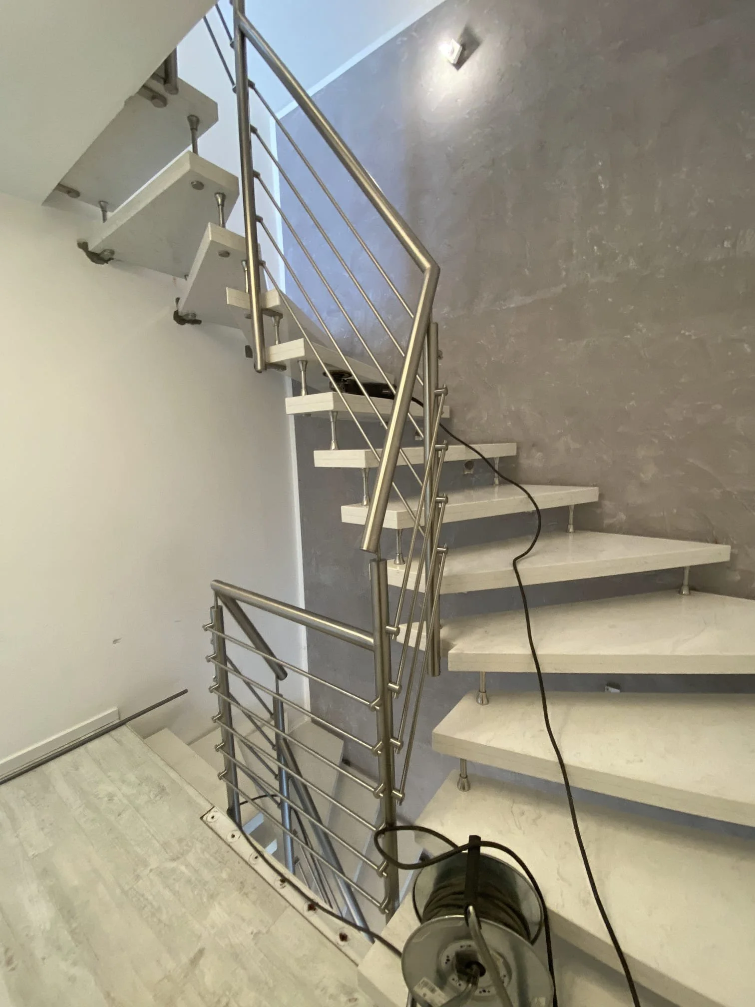 Edelstahl-Treppenhandlauf mit weißen Stufen in einem modernen Treppenhaus, im Hintergrund eine graue Wand