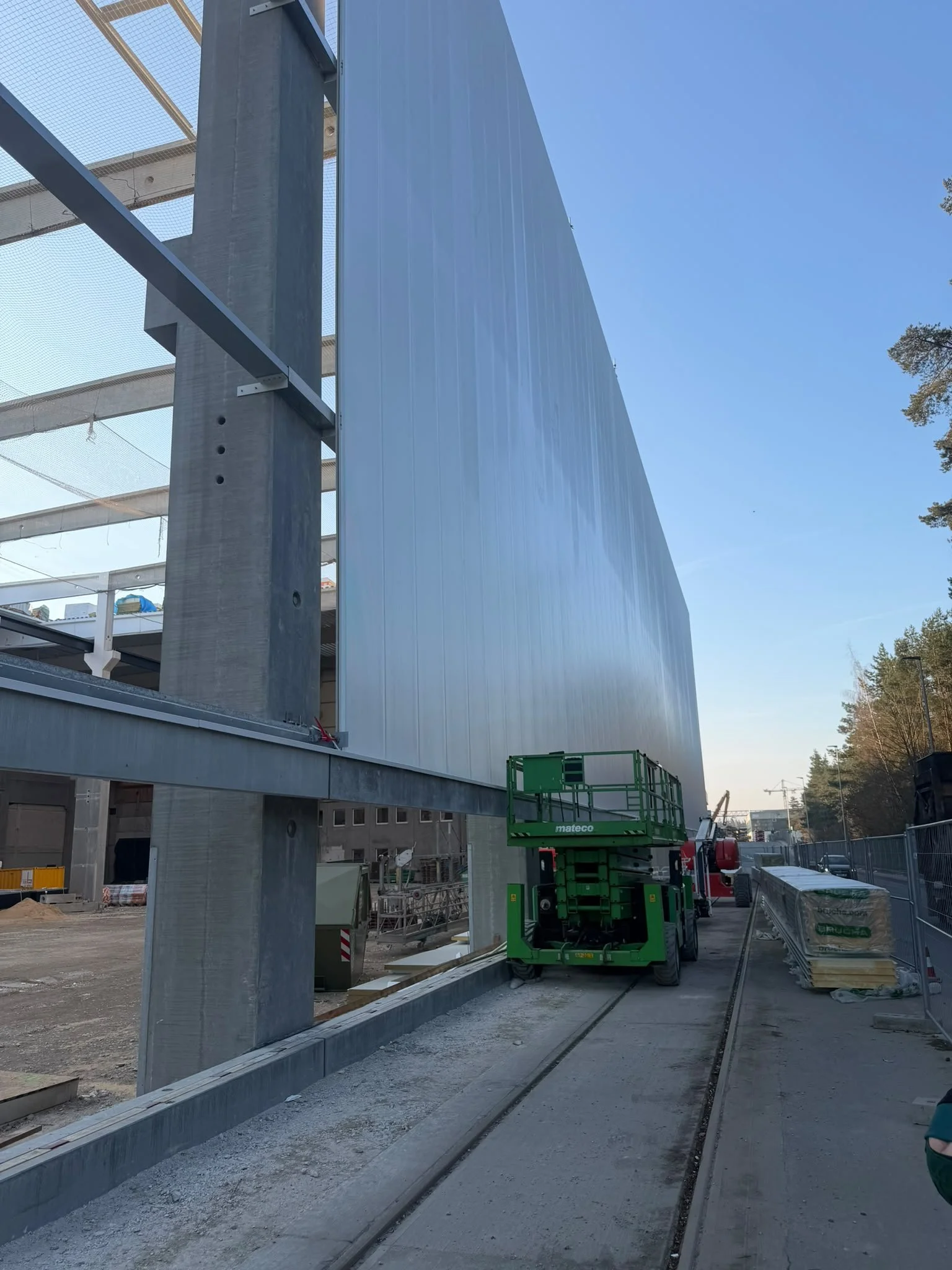 Baustelle mit Baustrommast, Kran, Baugerüst und Baumaschinen am Baufortschritt, Hintergrund mit Bäumen und Himmel.