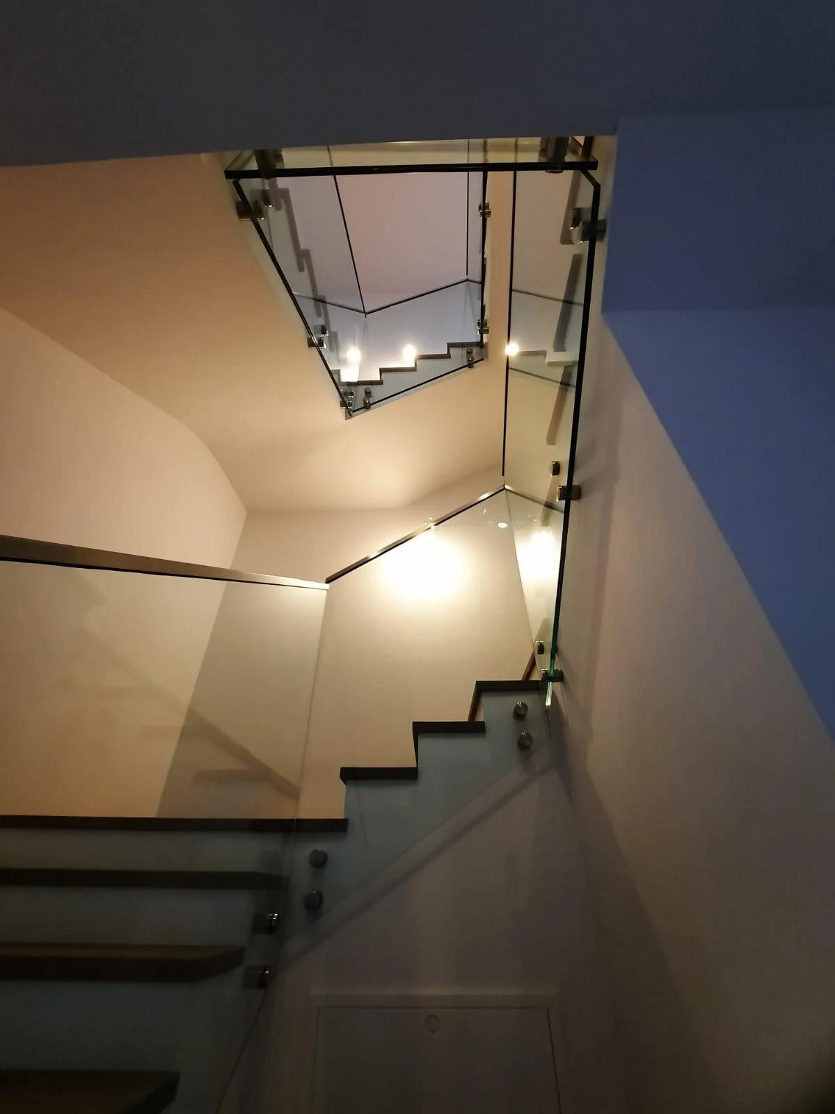 Innenansicht eines modernen Treppenhauses mit Glasgeländern und Deckenbeleuchtung.