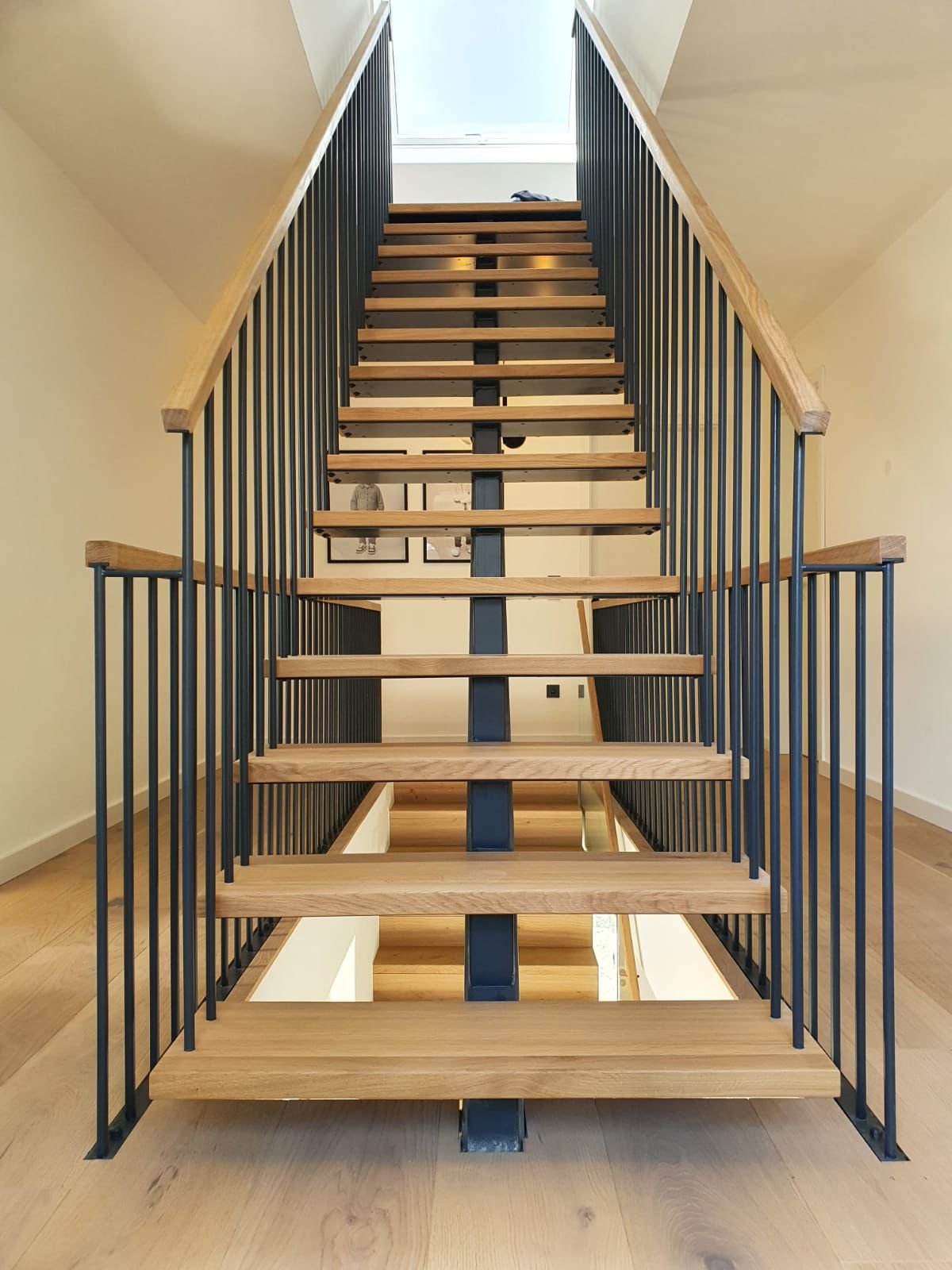 Leere Treppe mit schwarzen Geländern und Holzstufen, Blick nach oben, mit Fenster an der Decke.
