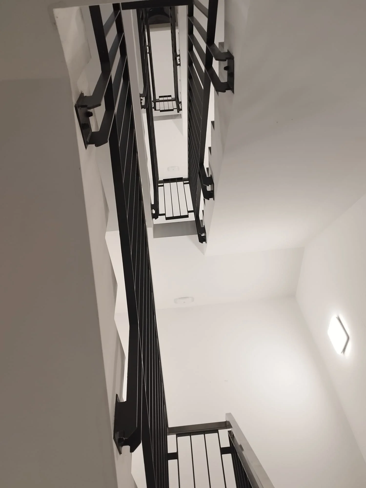 Blick nach oben auf eine Treppe mit schwarzen Geländern in einem weißen Raum.