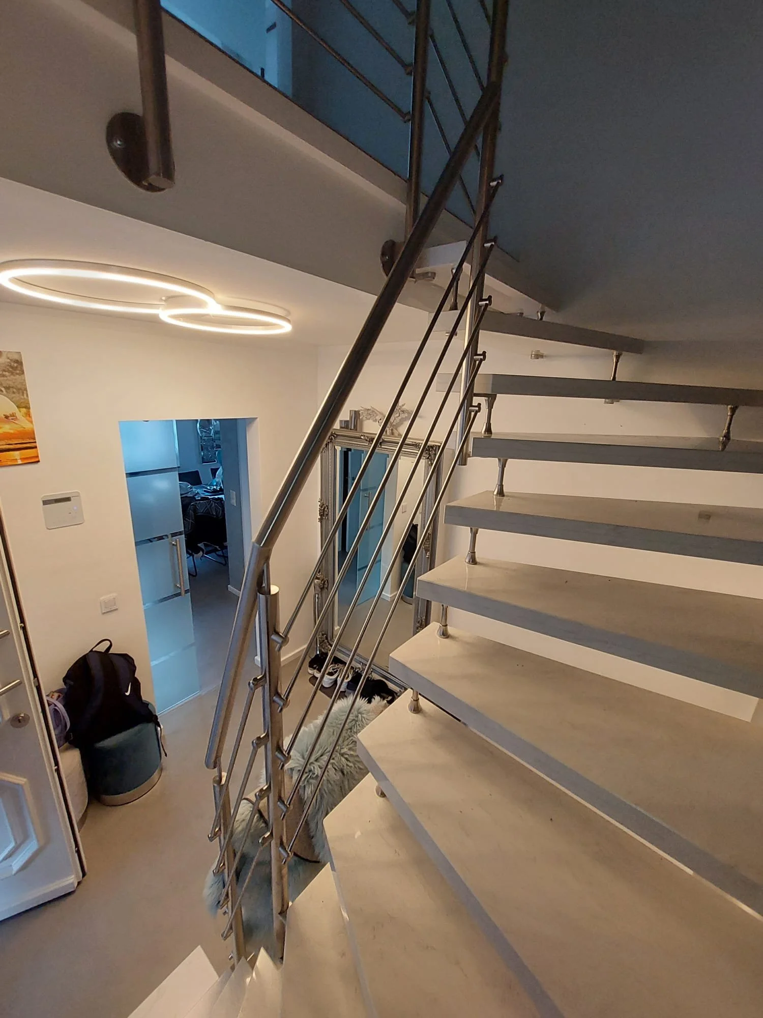 Innenansicht eines Treppenhauses mit offener Treppe, modernen Leuchten und mehreren Schuhen an der Wand. Im Hintergrund sind Räume sichtbar.