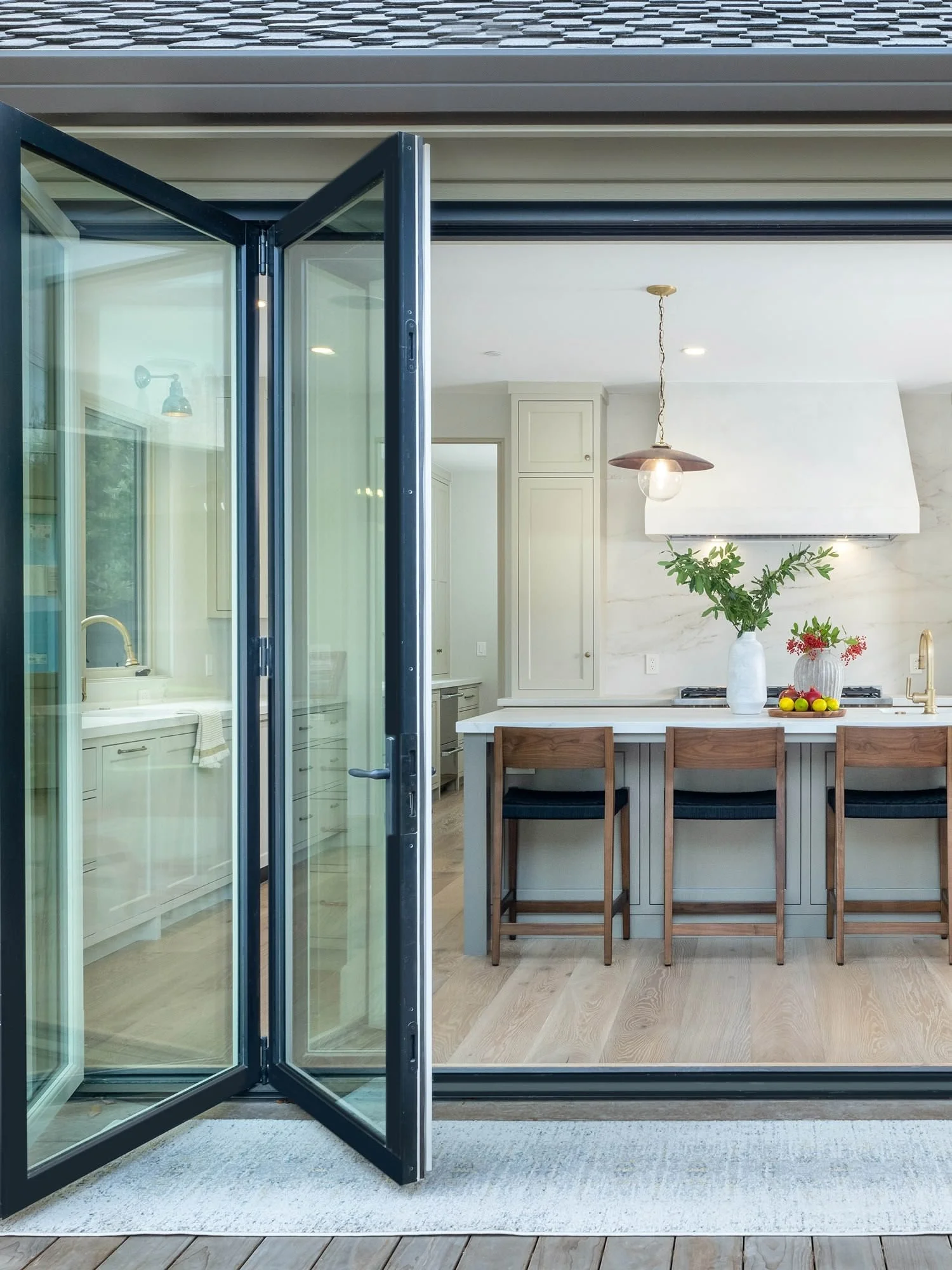 Open black-framed glass door leading from the interior of a house to an outdoor deck area with wooden flooring.