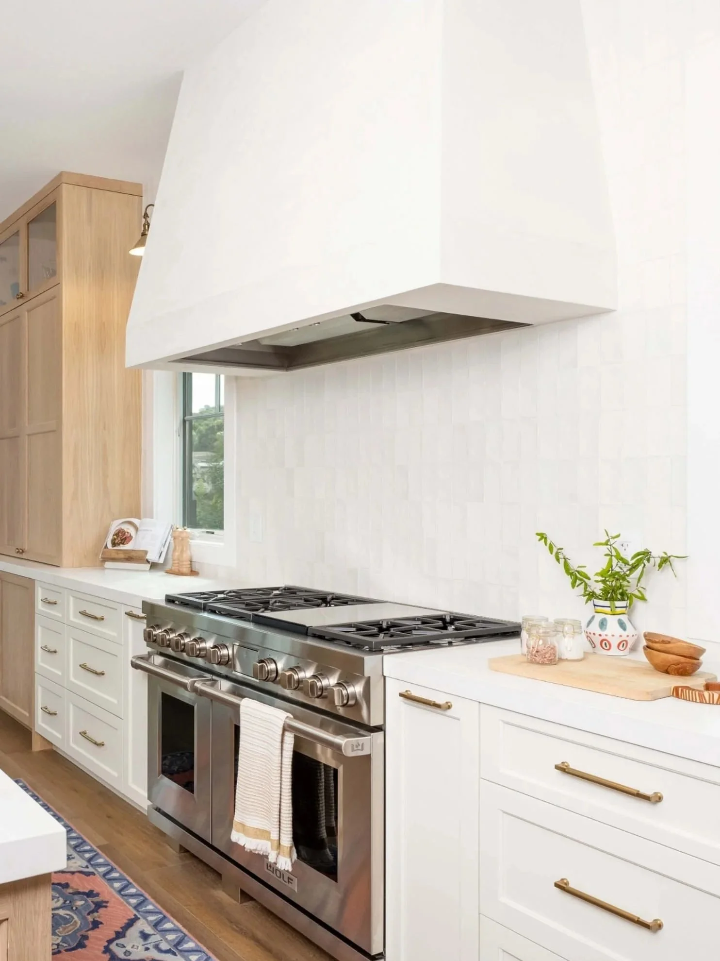 Modern kitchen with a stainless steel Wolf stove, white cabinets, a wooden countertop with bowls, jars, and a plant, and a white range hood.