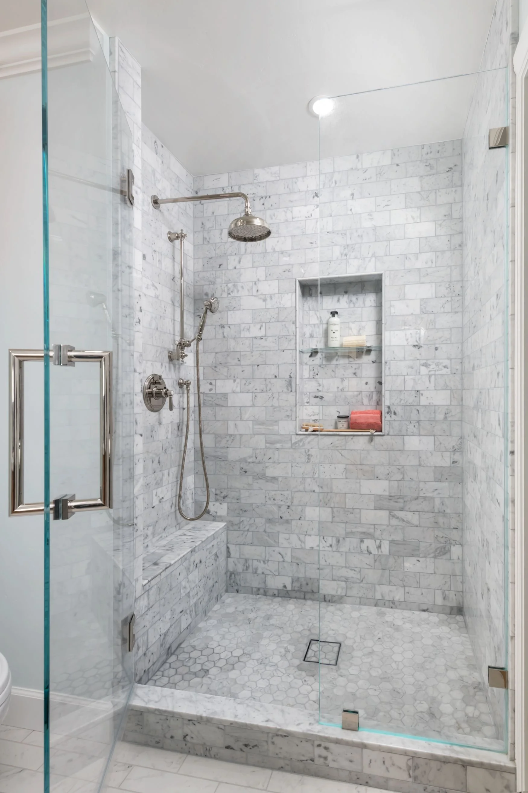 Carrara marble shower with polished nickel plumbing fixtures and glass door