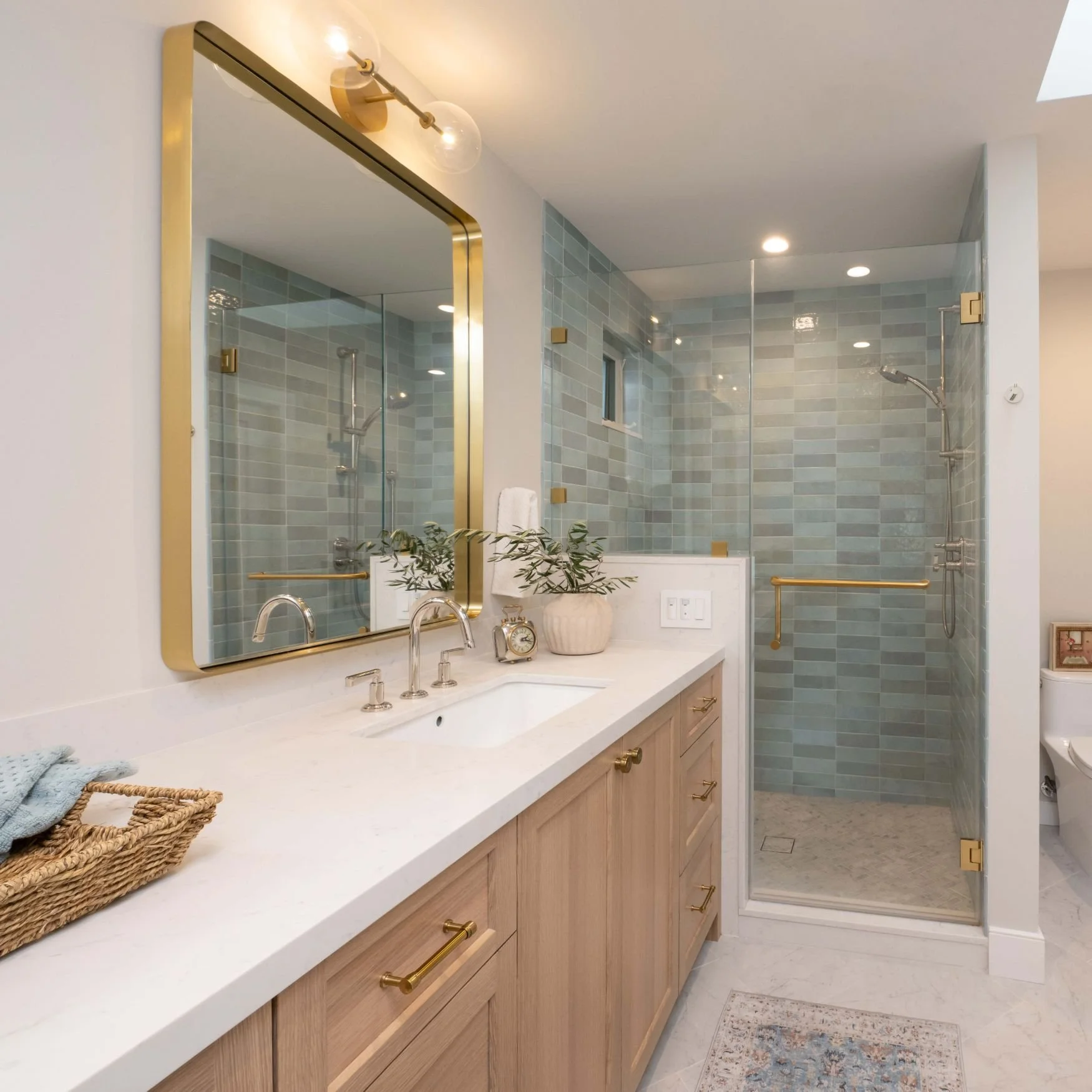 Large walk in shower with blue tiles and brass fixtures and oak vanity