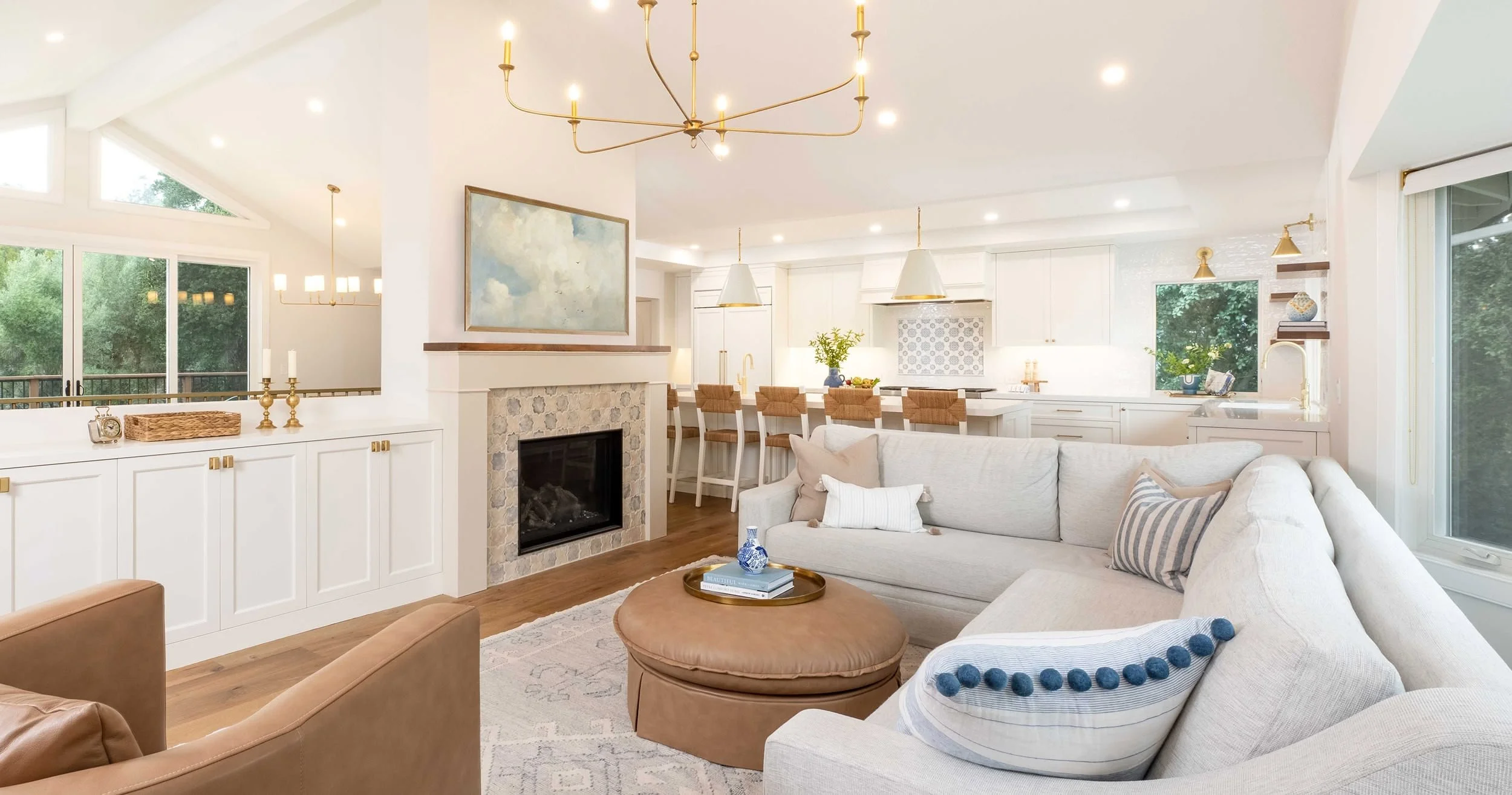 Open-concept living room and kitchen with white walls, hardwood floors, a fireplace, large windows, and modern decor.