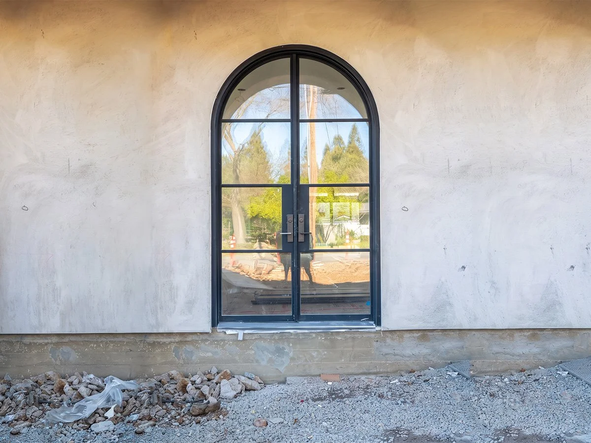 Finished exterior wall with a black arched window, construction debris and gravel in front.