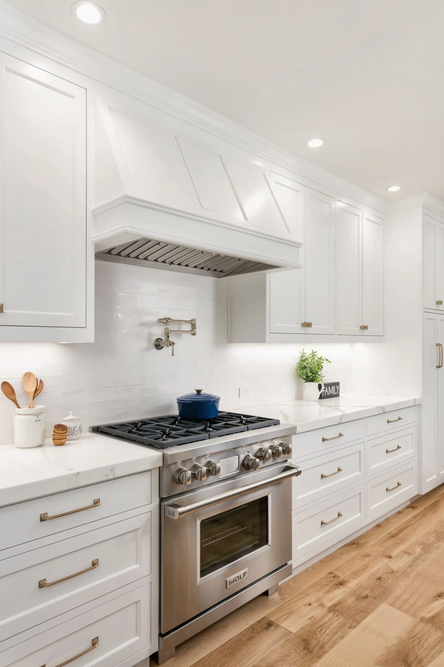 Stainless steel range with white cabinet hood and cabinets with oak flooring
