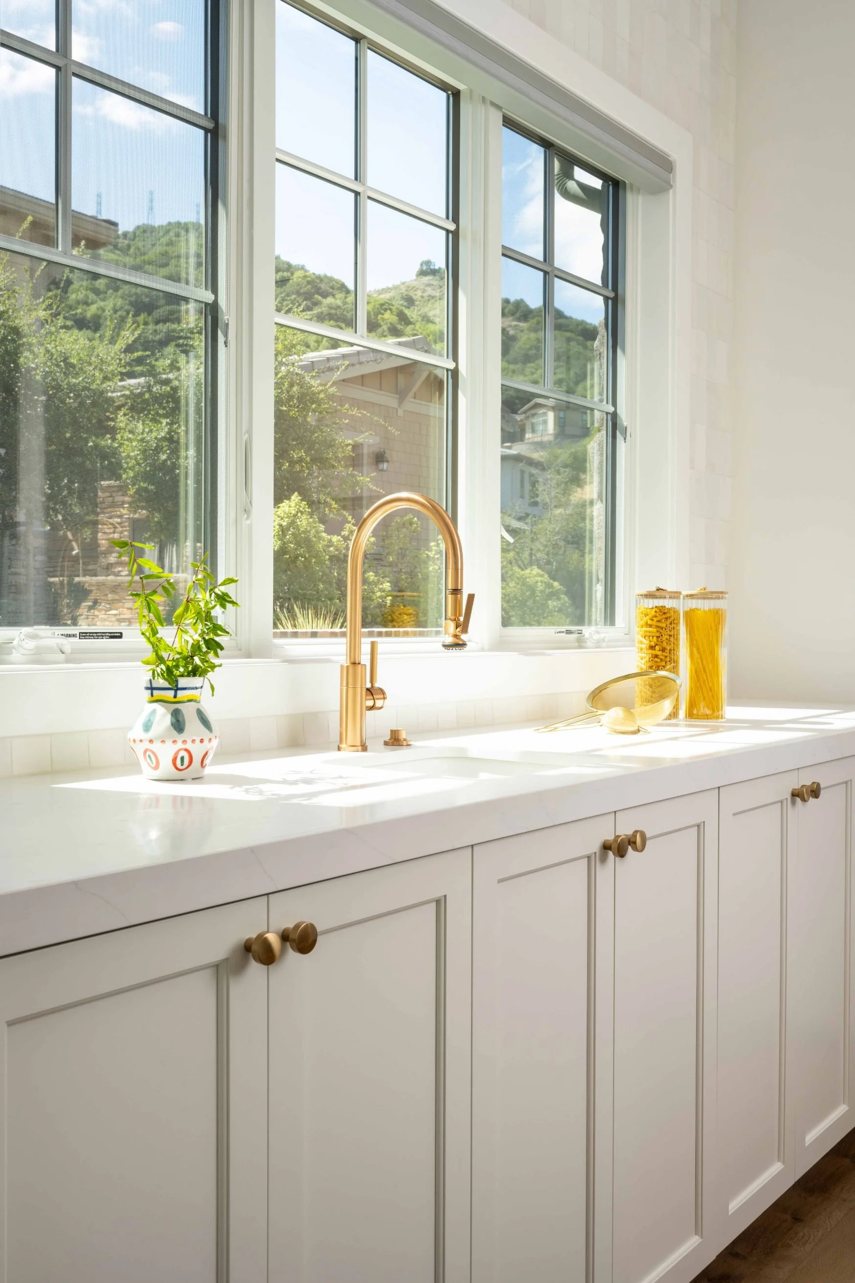 Large window with brass faucet and white cabinetry