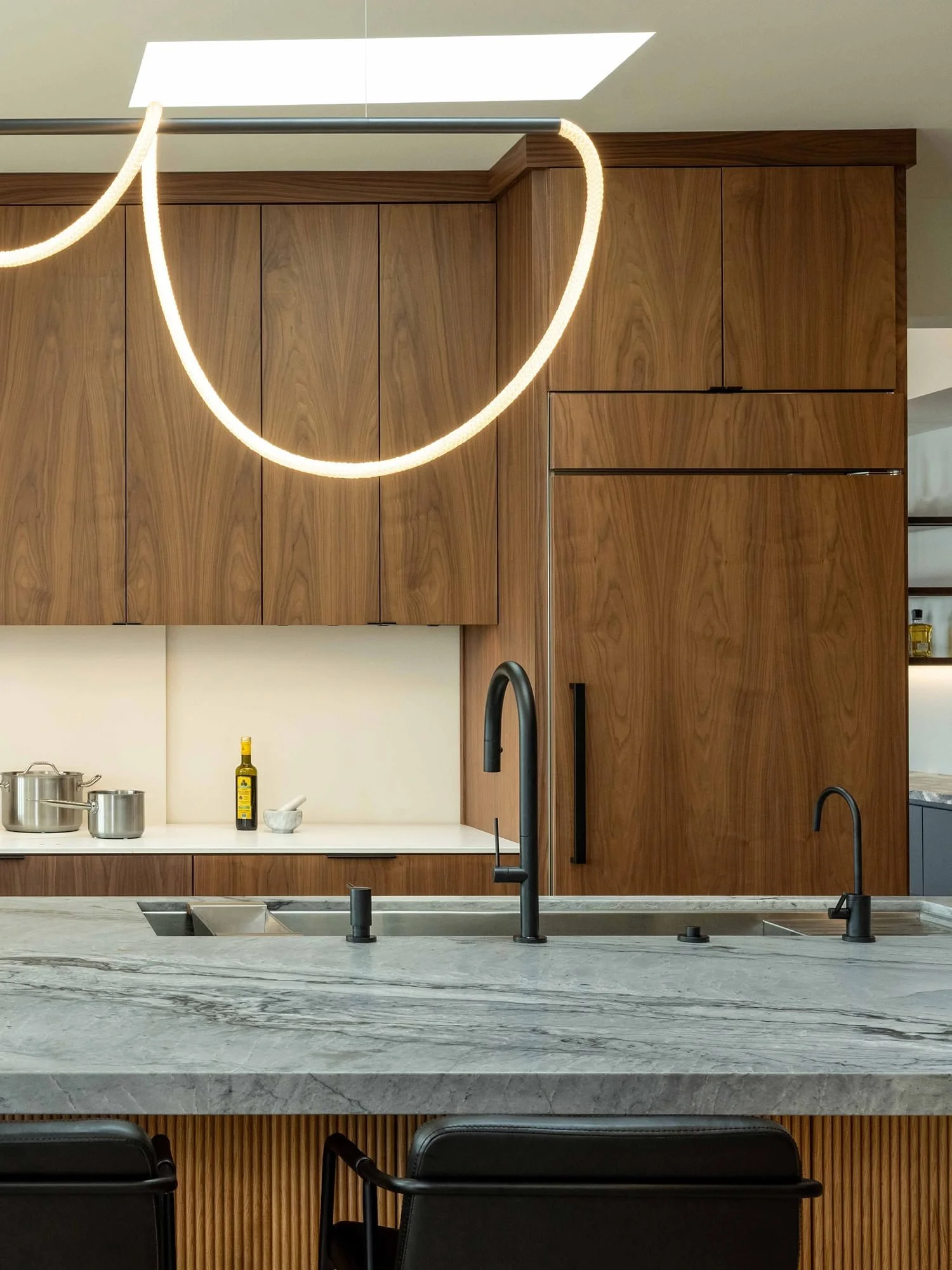 Modern kitchen with wooden cabinets, a marble countertop, and black fixtures. A pendant light with a circular design hangs above.