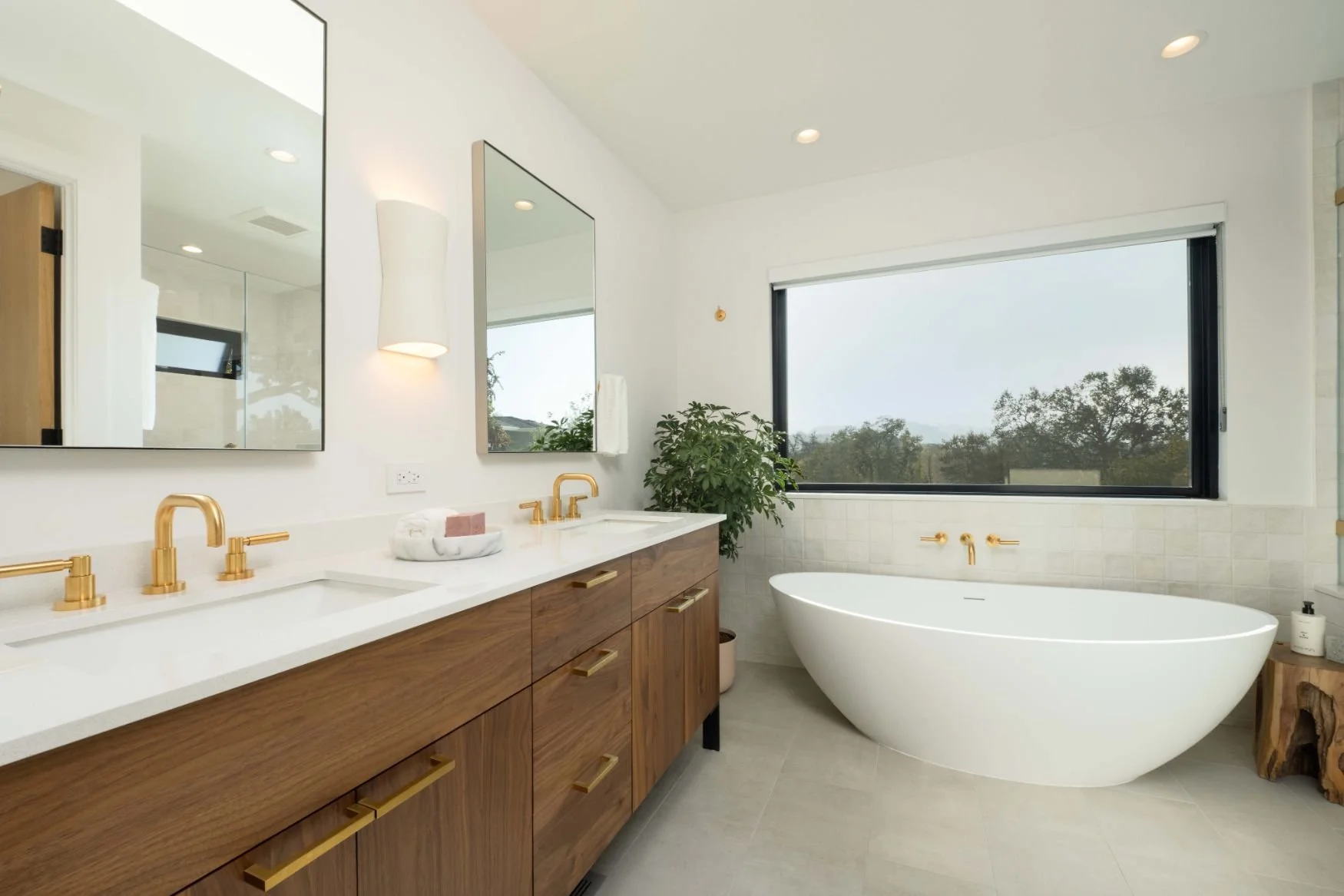 Bathroom with walnut vanity, gold fixtures, freestanding tub under large window
