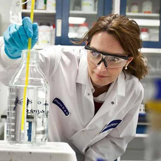 Female scientist in safety goggles and lab coat performing a liquid measurement experiment in a laboratory.