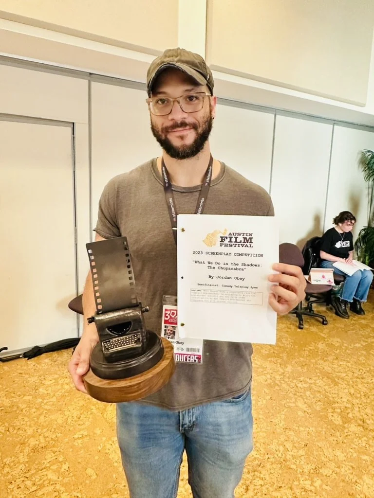 A man holding a trophy and a certificate at the 2023 Custom Film Festival, celebrating his screenplay titled 'What We Do in the Shadows: The Chupacabra'.