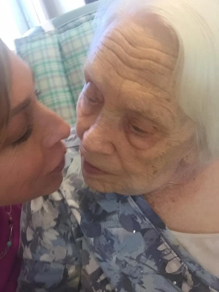 A young woman and elderly woman face each other closely, about to kiss, in an intimate moment.