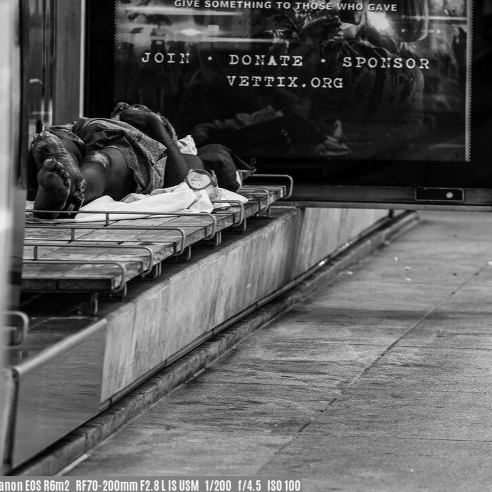 The gentleman in this CTA bus shelter made a bed, lying across the bench's rails. He was not wearing shoes or socks, and he had a clubbed foot.
