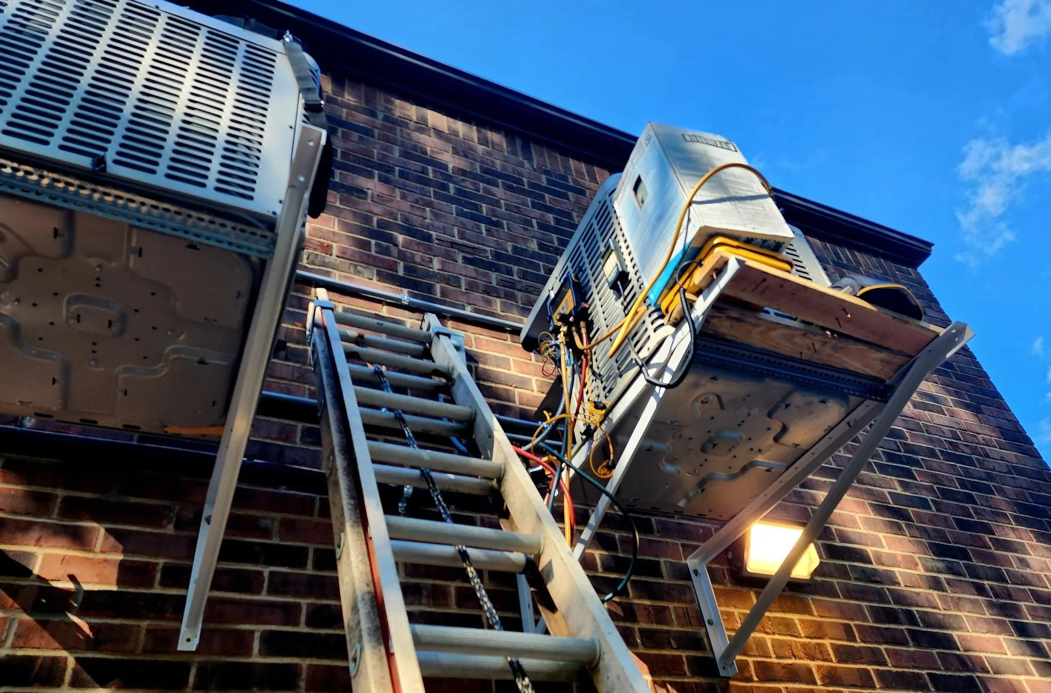 Ladder and HVAC units installed outside a brick building, with a clear blue sky in the background.