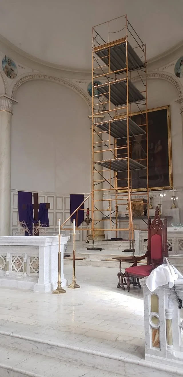 Interior of a church with a large scaffold set up in the center, surrounded by religious artifacts and furniture.