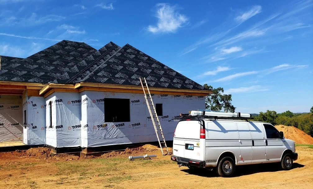 Construction site with a house in progress and a white work van parked nearby.