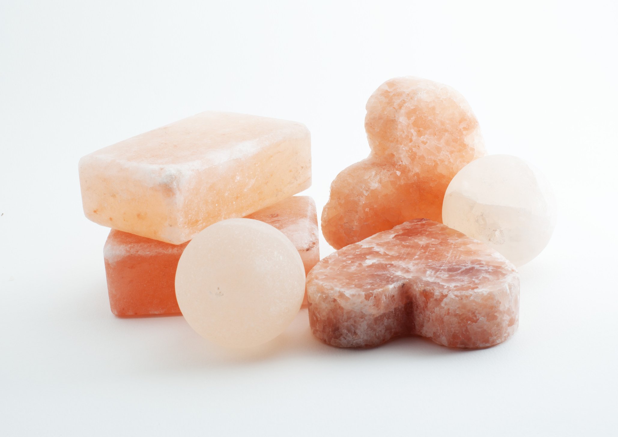 A collection of pink and white Himalayan salt rocks and salt balls on a white background.
