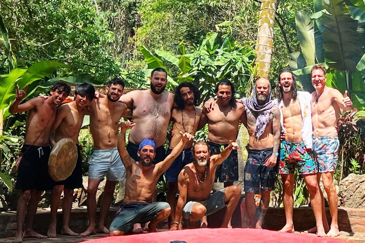 Group of shirtless men posing together in a lush tropical jungle.