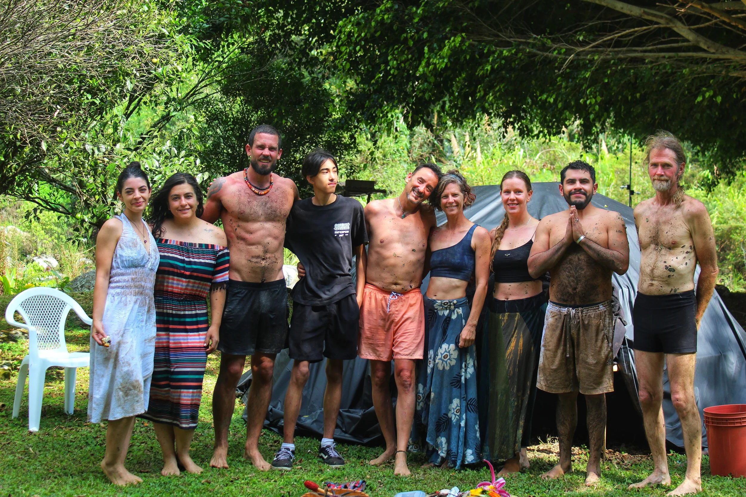 Group of 10 adults posing outdoors in a lush forest beside a tent