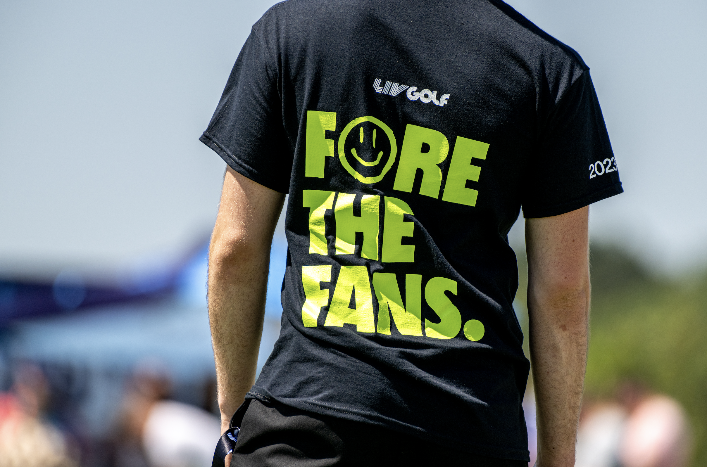 Person wearing a black t-shirt with bright green and white text, during daytime outdoor event.