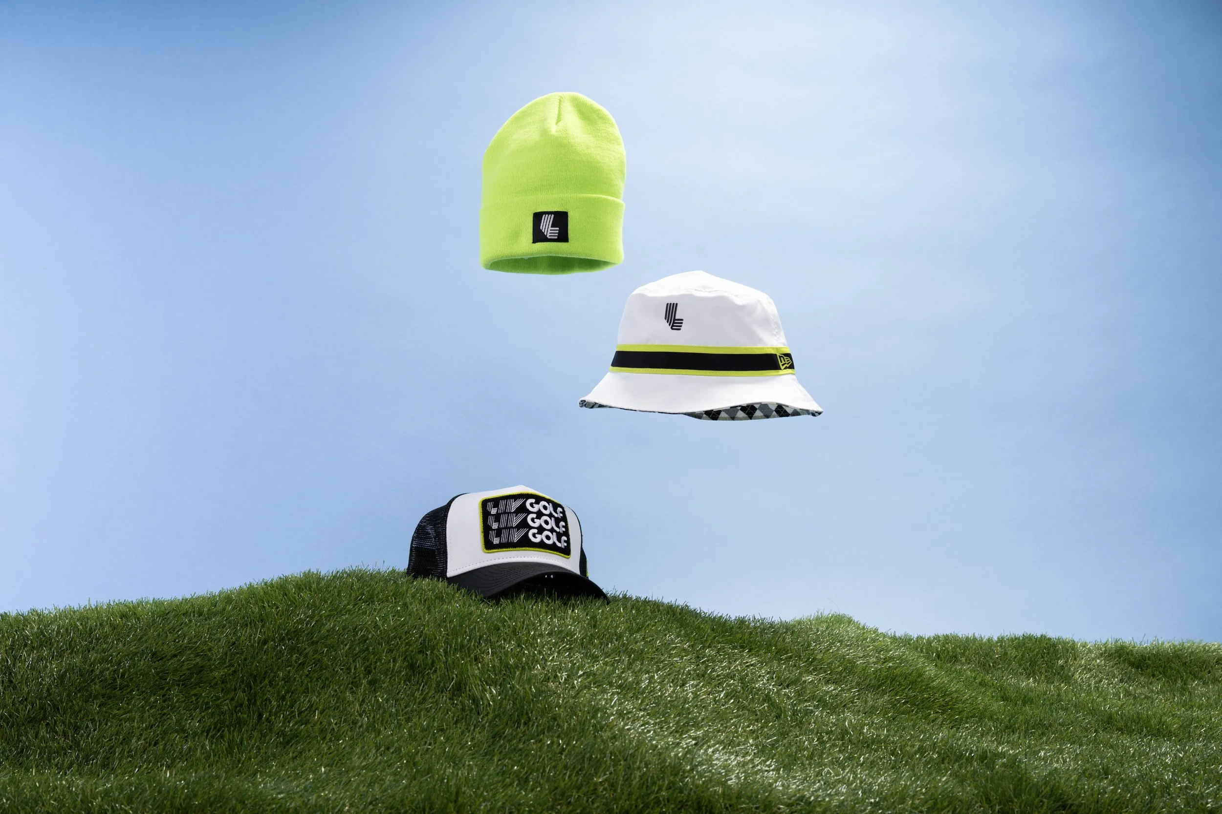 Four golf hats are floating above a grassy hill against a clear blue sky.
